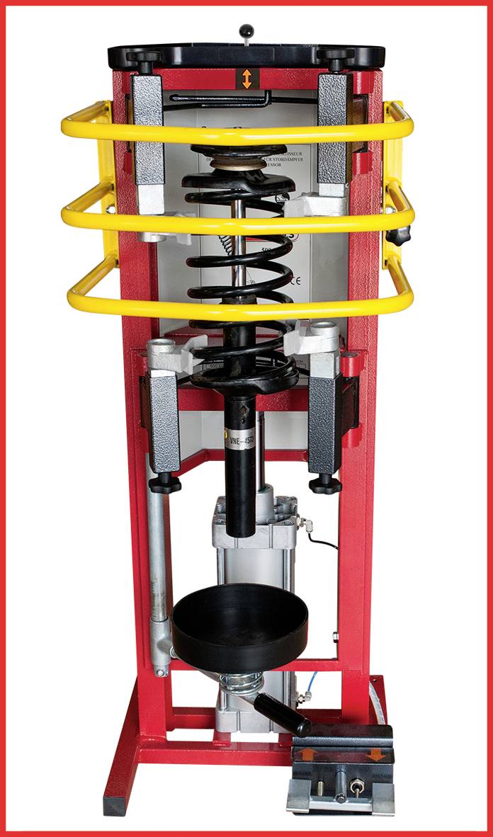 Pohled zepředu na hydraulický zkušební stojan pro zpětný ráz s žlutými bezpečnostními oblouky a červeným rámem, určený pro testování tlumičů.