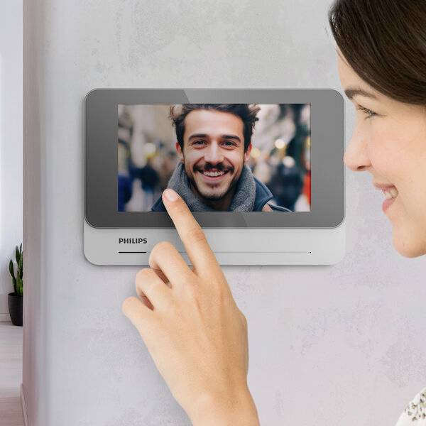 Osoba obsluhuje interkomový systém Philips s displejem, na kterém je vidět usmívající se osoba.
