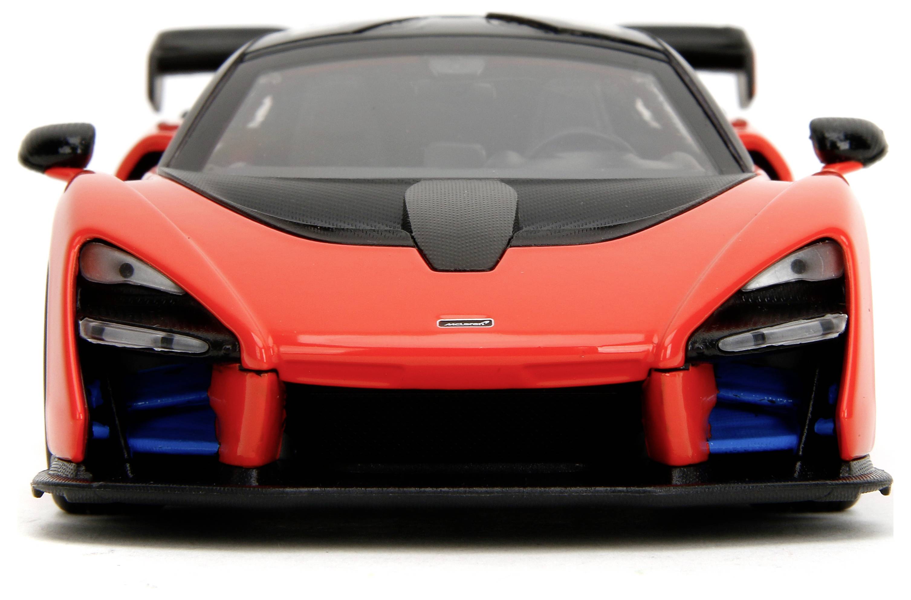 Červené modelové auto v popředí, sportovní vůz s černými akcenty a aerodynamickým designem, na bílém pozadí.