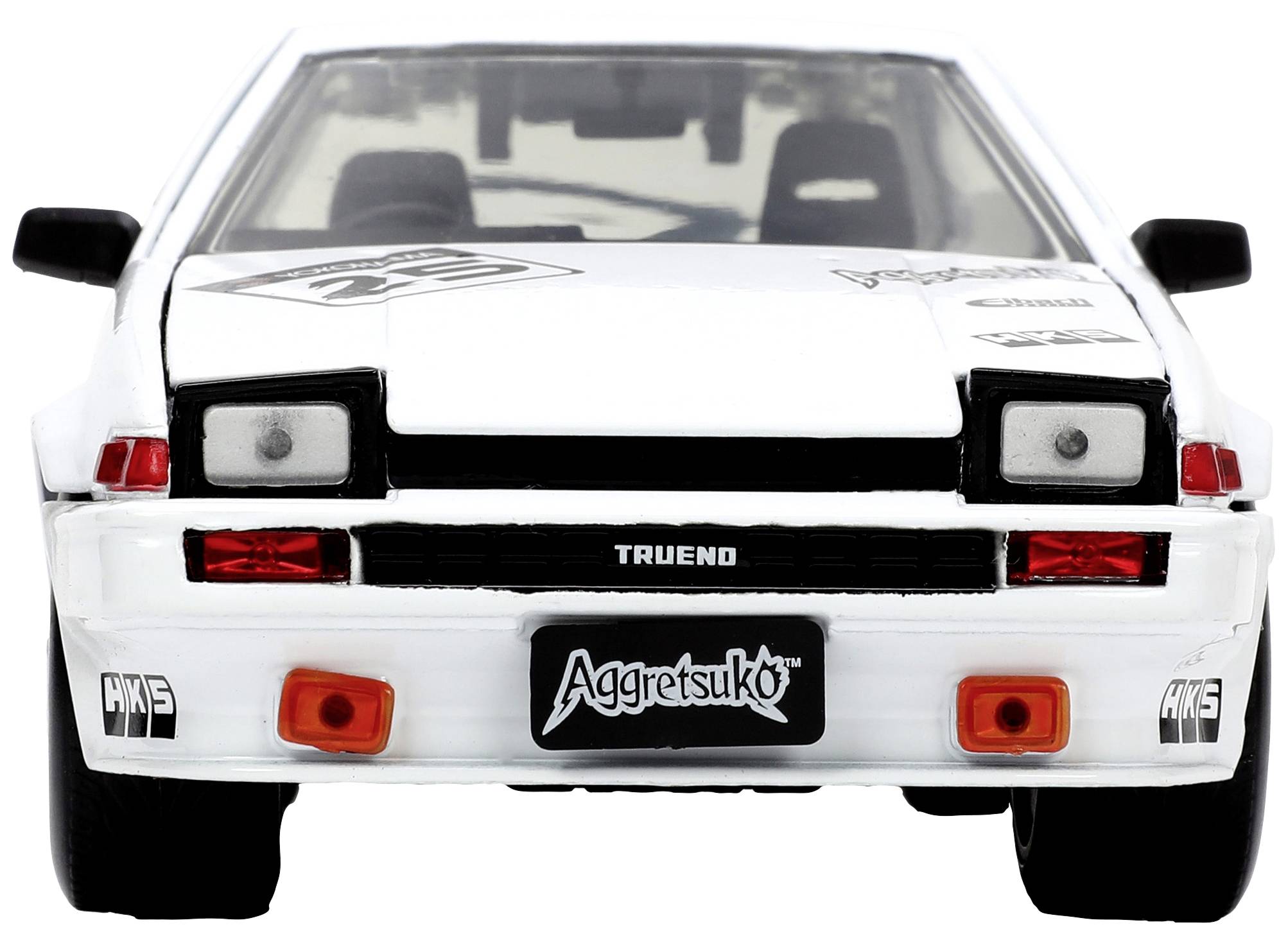 Bílé auto s nápisem 'Trueno' na předním nárazníku, které má poznávací značku s motivem 'Aggretsuko'.