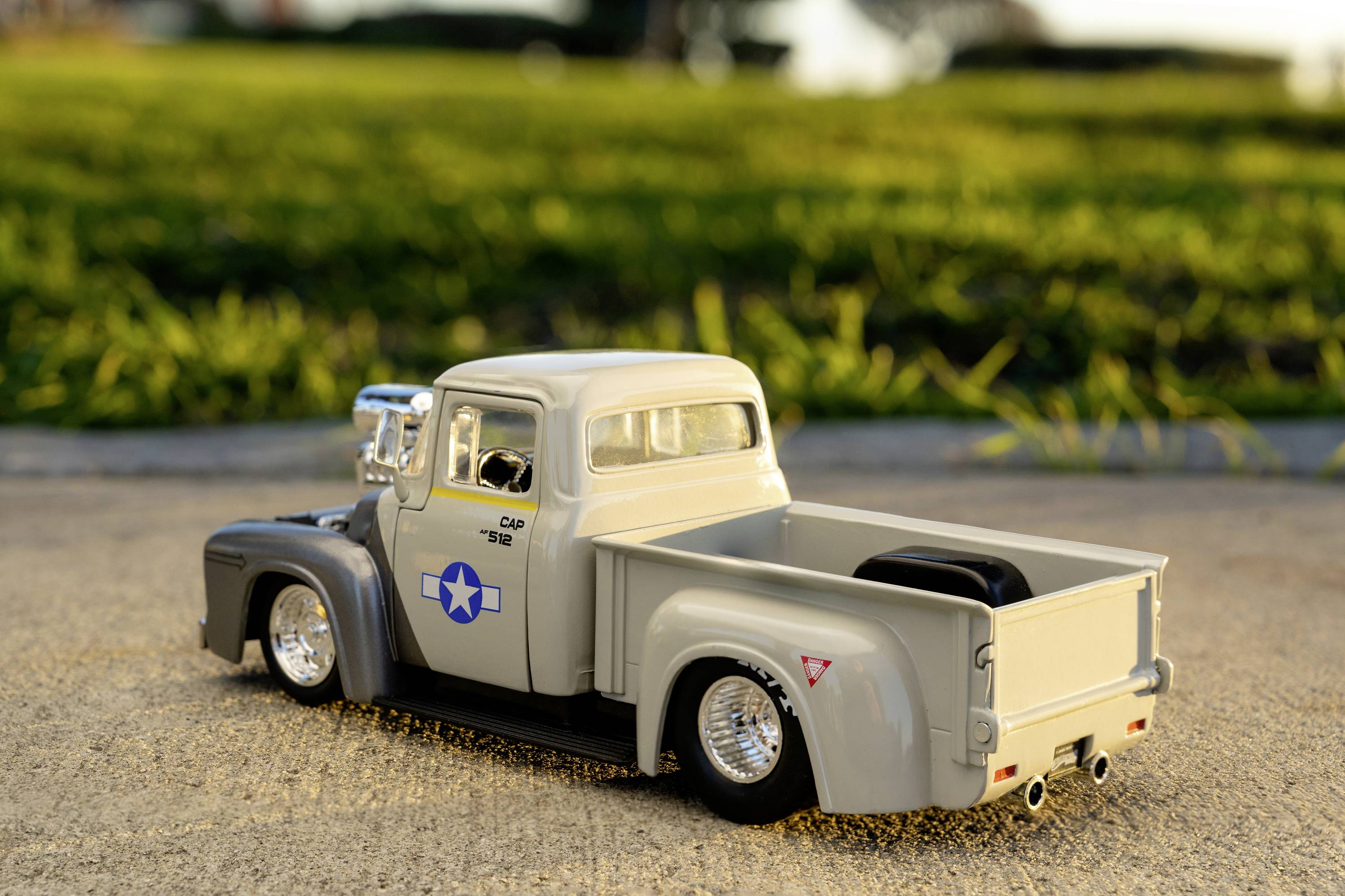 Model starého šedého pickupu stojí na chodníku před loukou. Truck má modré emblém ve tvaru hvězdy.