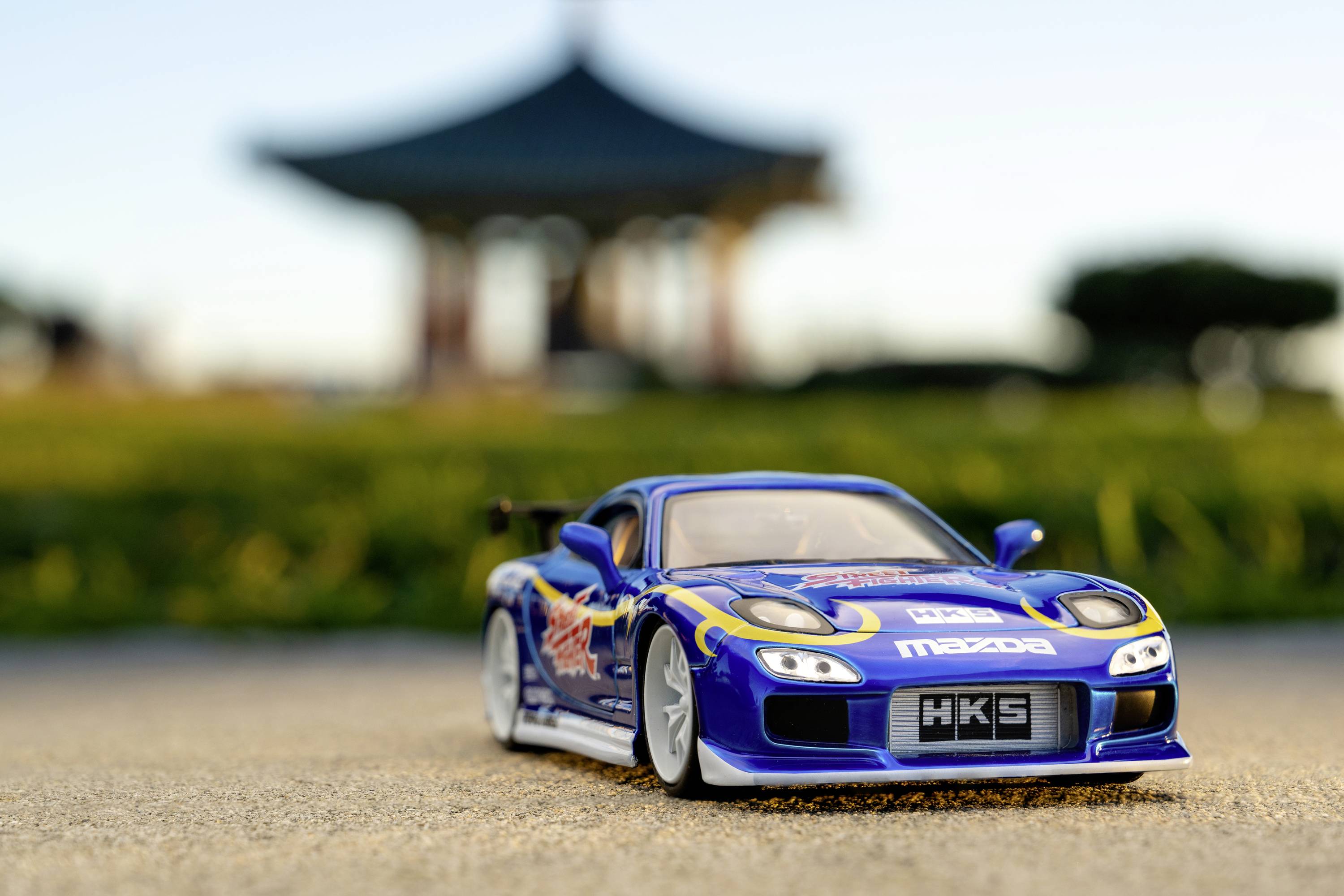 Hračkářské modelové autíčko v modré barvě na betonovém povrchu, pozadí rozmazané; symbolizuje rychlost a lásku k motorsportu.