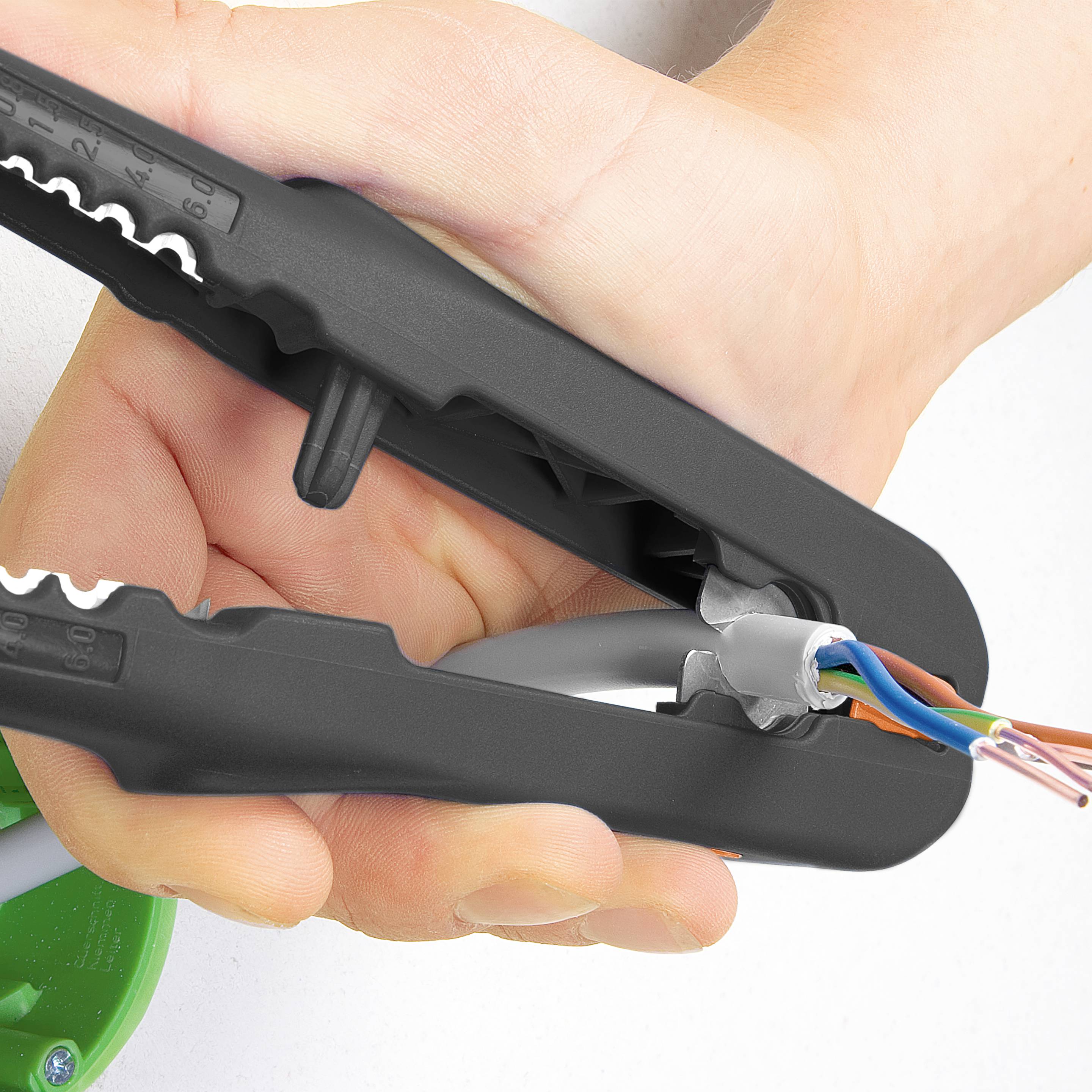 Osoba drží černý odizolovací nástroj a pomocí něj odstraňuje plášť šedého kabelu, aby odhalila vnitřní vodiče.