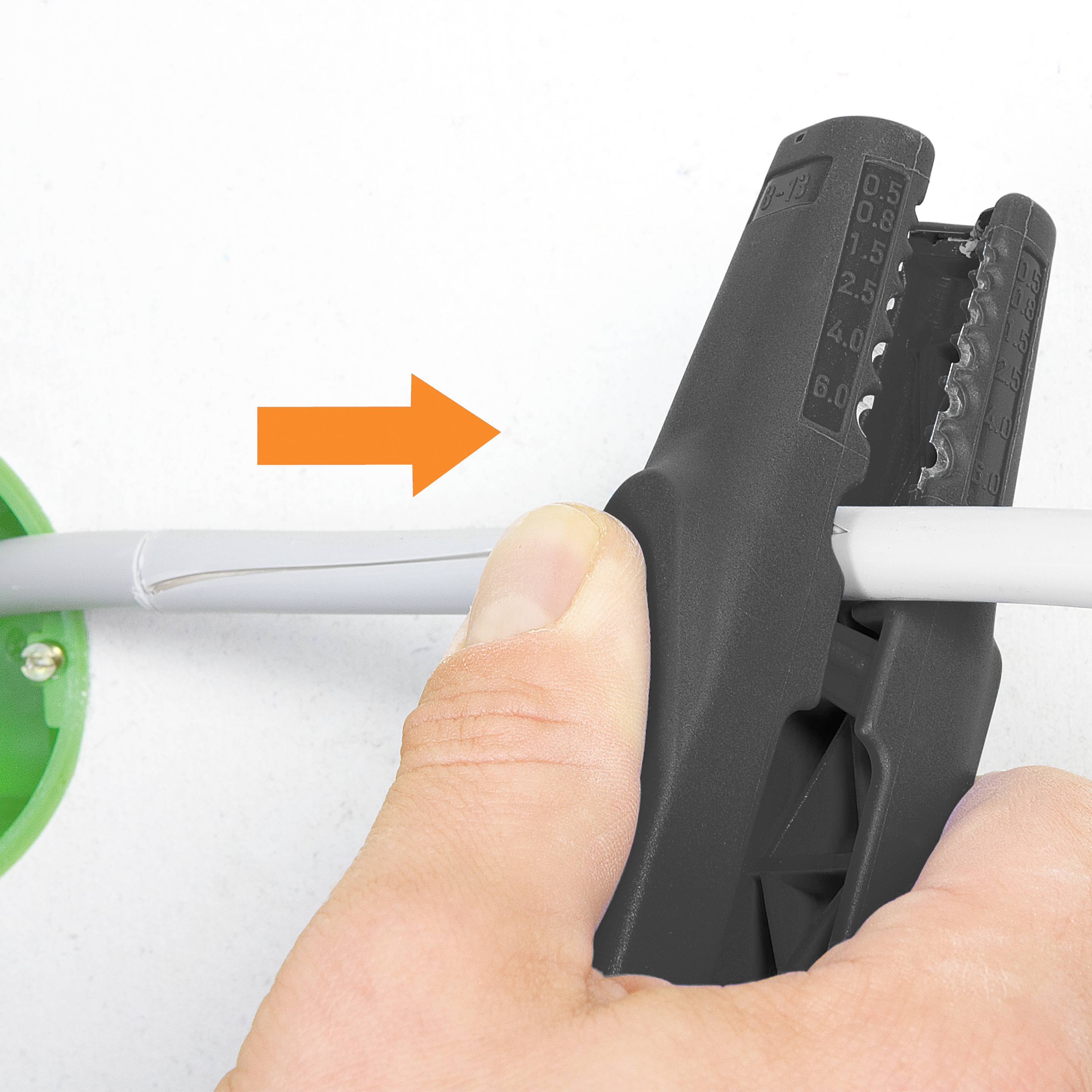 Jedna ruka drží černé štípací kleště a stříhá bílý kabel. Oranžový šipka ukazuje na kabel.