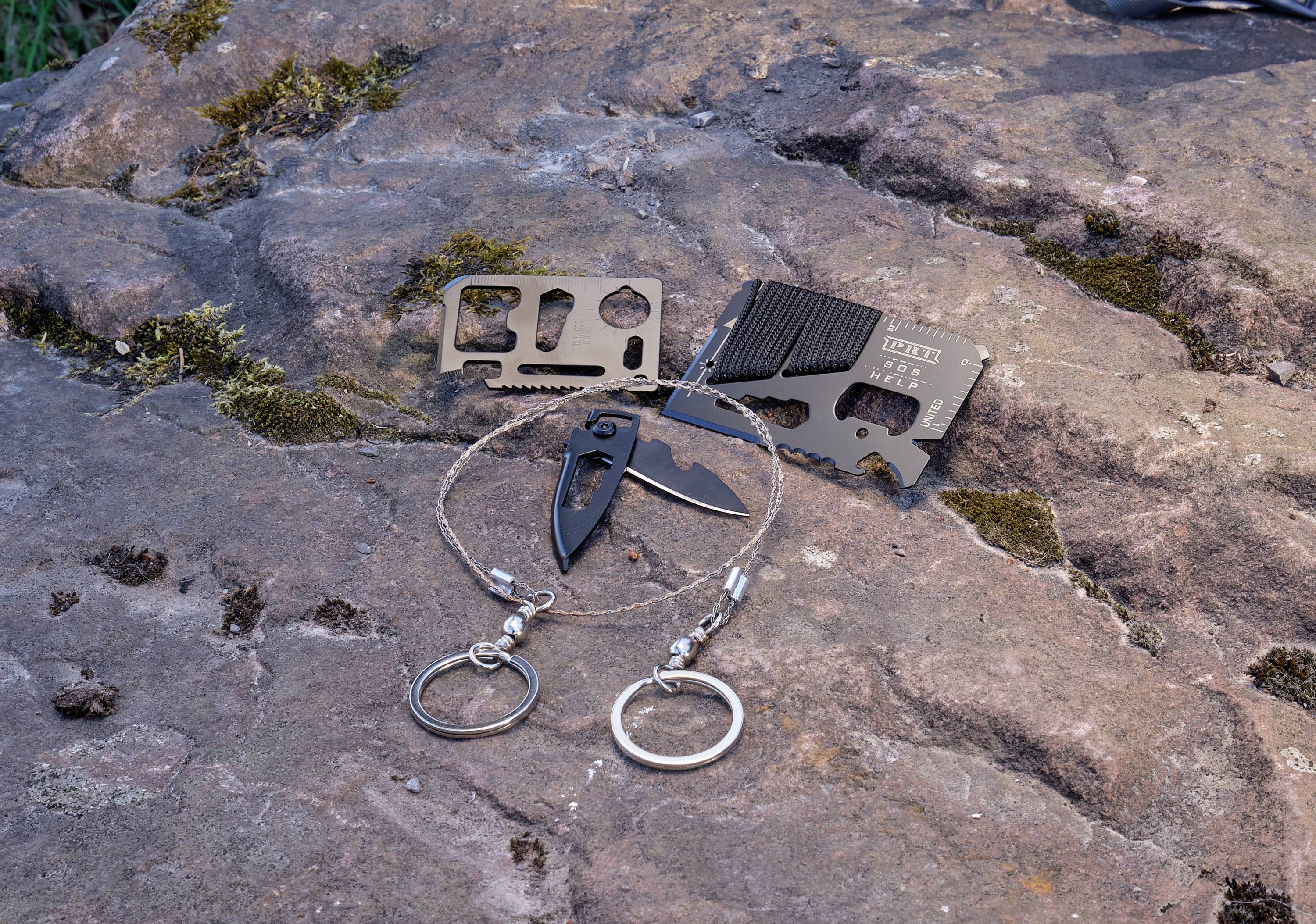 Nástroje pro přežití leží na skále, včetně multifunkční karty, kapesního nože a drátěné pily.