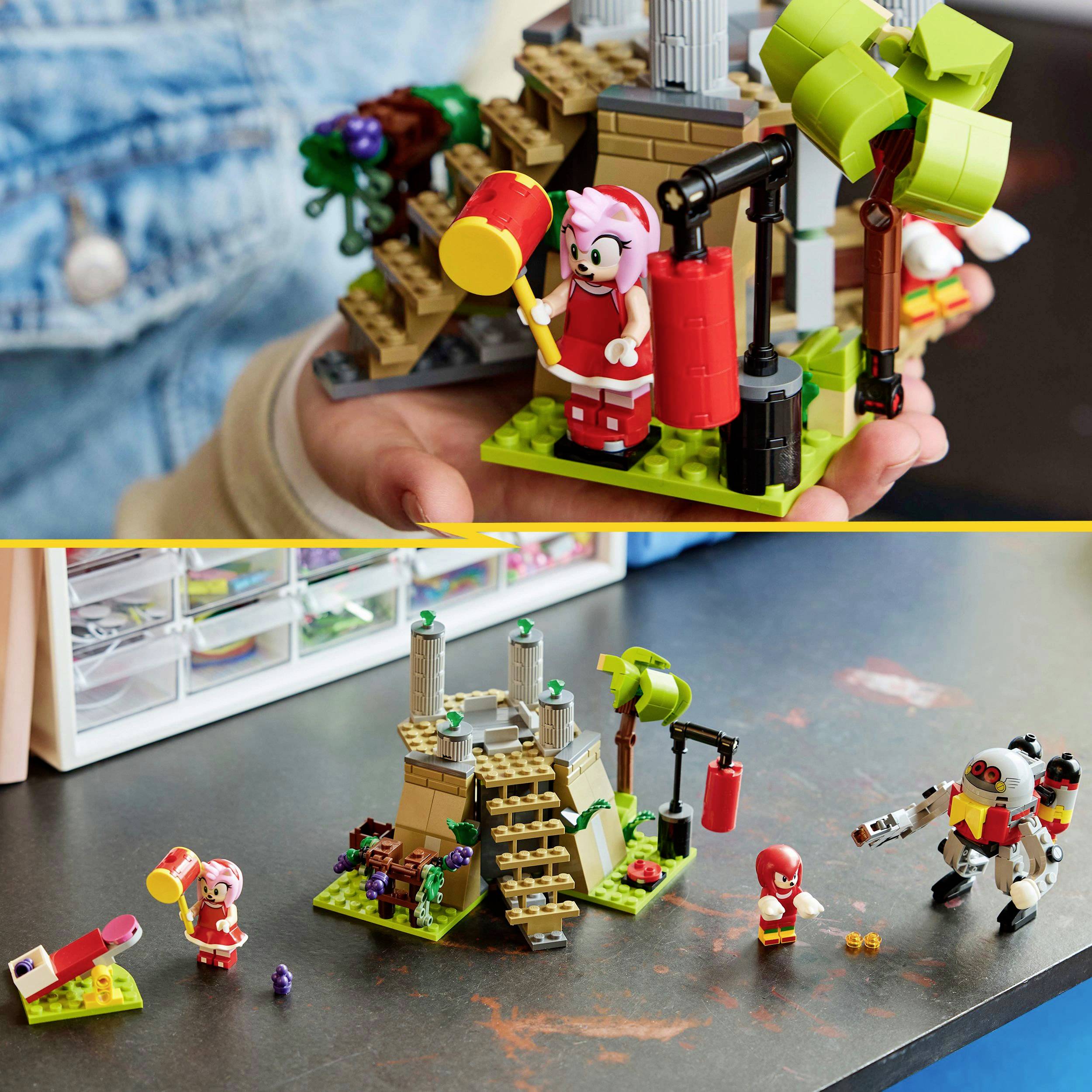 Jedna ruka drží Lego soupravu s růžovou figurkou. Na stole stojí sestava s palmami, schody a postavičkami.