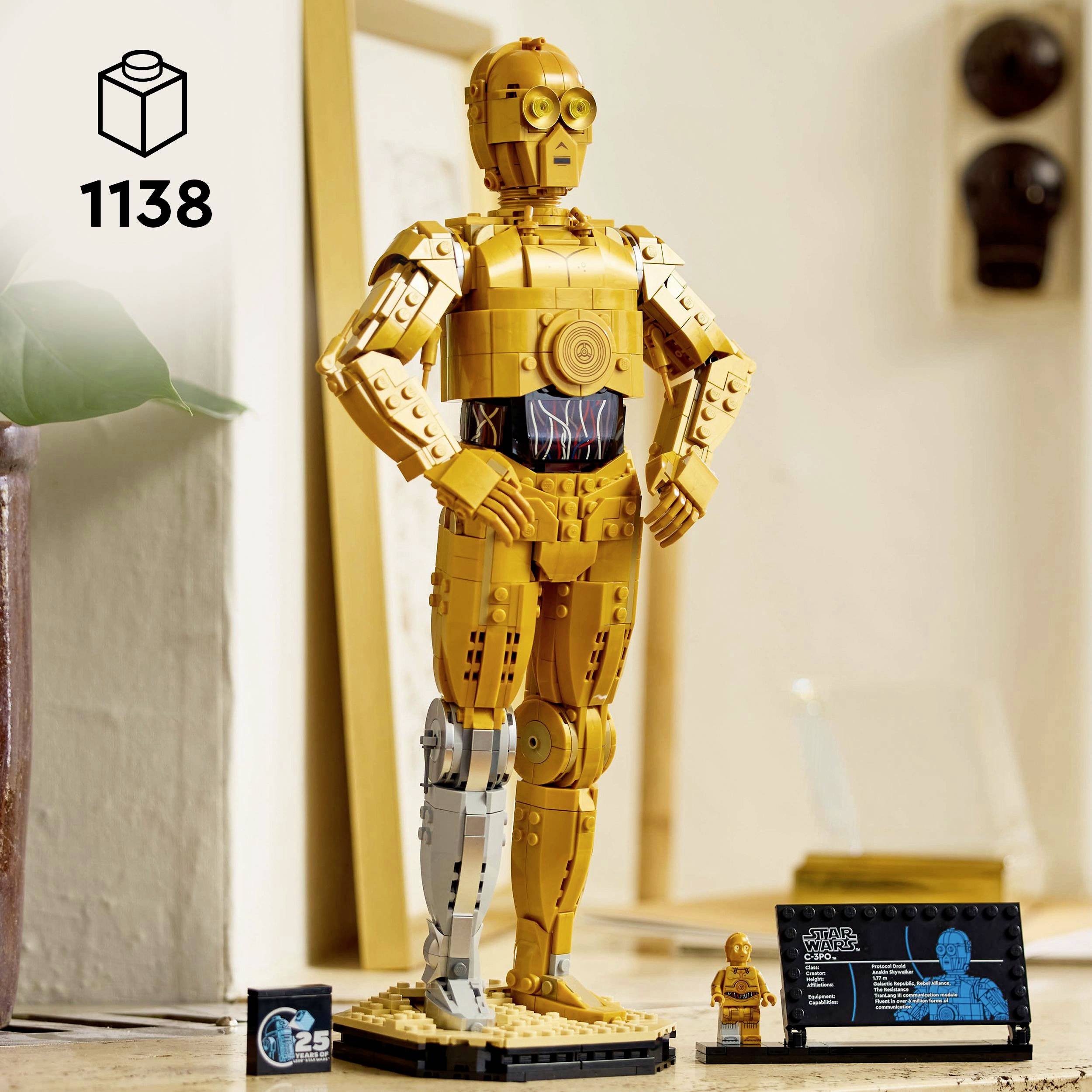 Žlutý robot složený z kostek stojí na stole vedle své miniaturní verze. V pozadí je krabice s čísly '1138'.