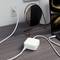 Bílý adaptér je připojen do elektrické zásuvky. Do adaptéru je zapojen kabel od smartphonu. V pozadí je viditelný notebook.