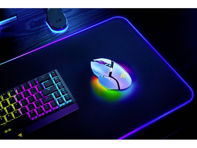 Bílá herní myš a podsvícená klávesnice na RGB podložce pod myš, všechny s měnícím se barevným LED osvětlením na tmavém stole.