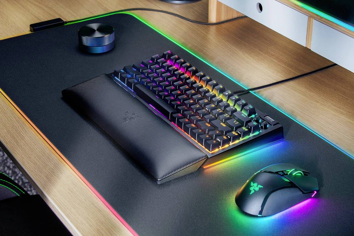 Počítačová klávesnice a myš s RGB podsvícením na pracovním stole. Osvětlení ukazuje přechod pestrobarevných barev.