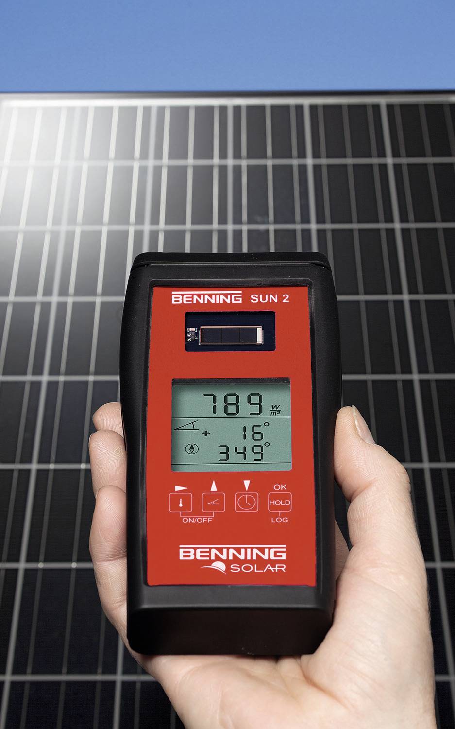 Jedna ruka drží solární měřicí přístroj před solárním panelem. Display ukazuje 789 W/m².
