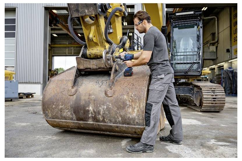 Mechanik používající elektrický nástroj k údržbě kýble velkého bagru v dílně na údržbu.