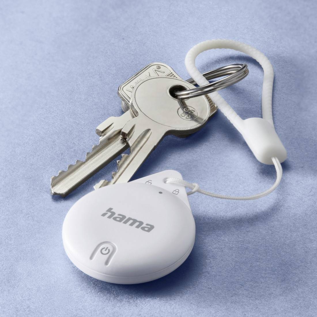 Malý bílý lokalizátor klíčů s logem 'hama' je připevněn ke klíčence se dvěma klíči a poutkem.