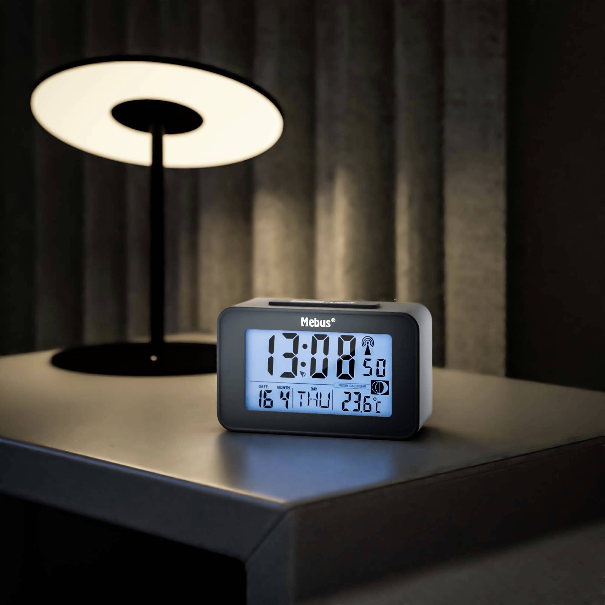 Digitální budík na stole ukazuje čas 13:00, datum 16. dubna, den čtvrtek a teplotu 23,6 °C. V pozadí stojí stolní lampa.
