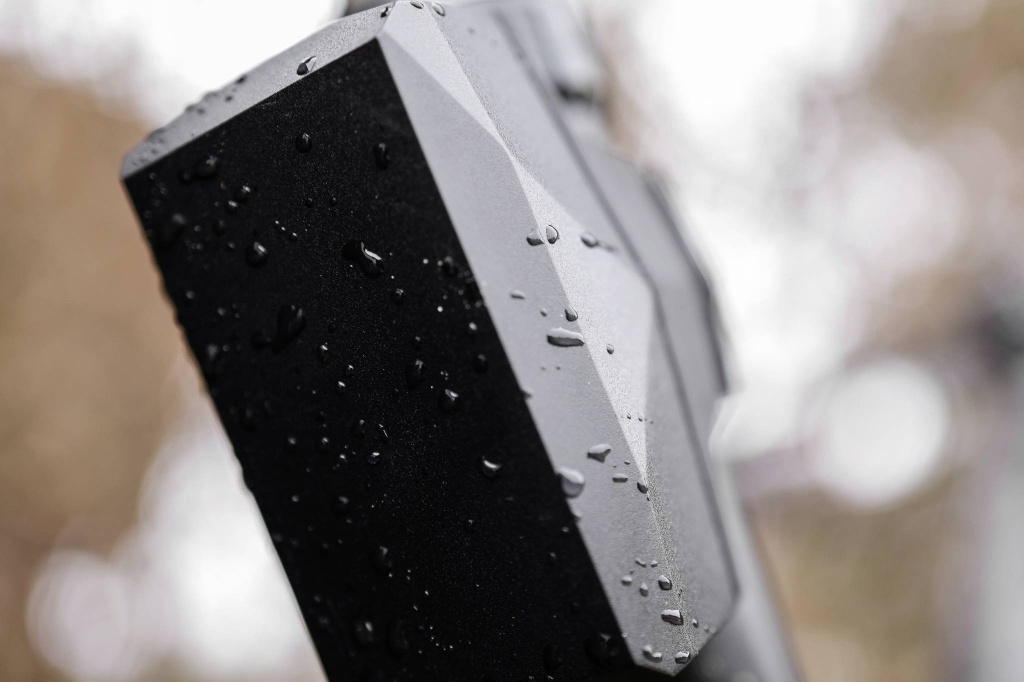 Detailní záběr černého obdélníku pokrytého deštěm s geometrickými tvary, rozmazané pozadí v teplých barevných tónech.