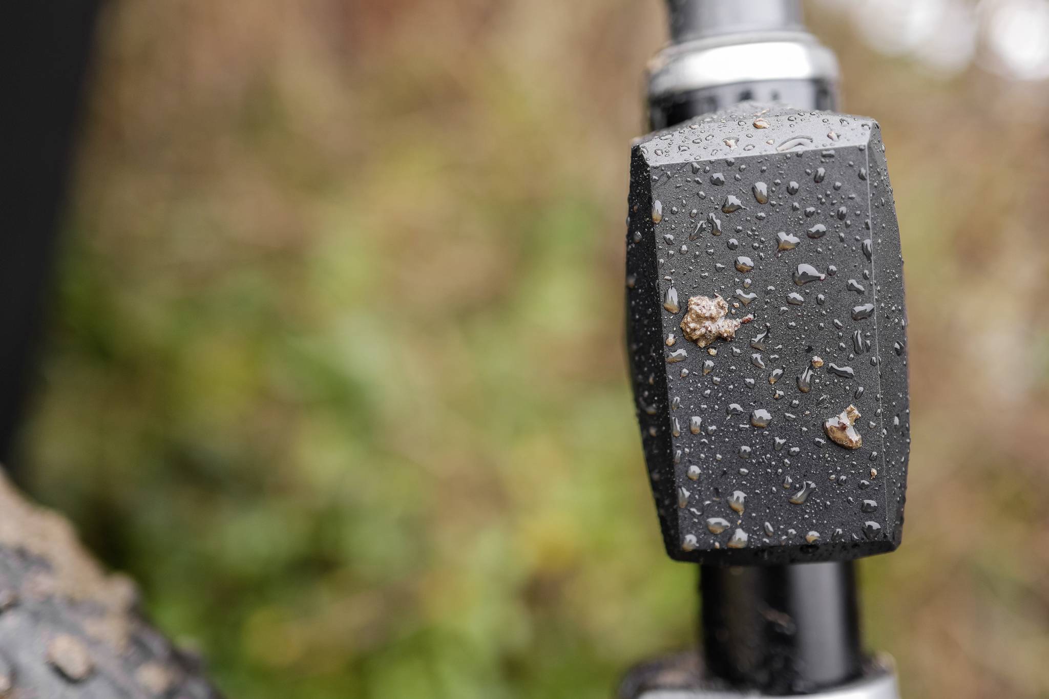 Detailní záběr řídítek jízdního kola s kapkami deště, v pozadí rozmazaná zeleň.