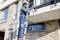 Dělník v modré kombinéze stojí na žebříku a opravuje balkon na moderní cihlové budově.