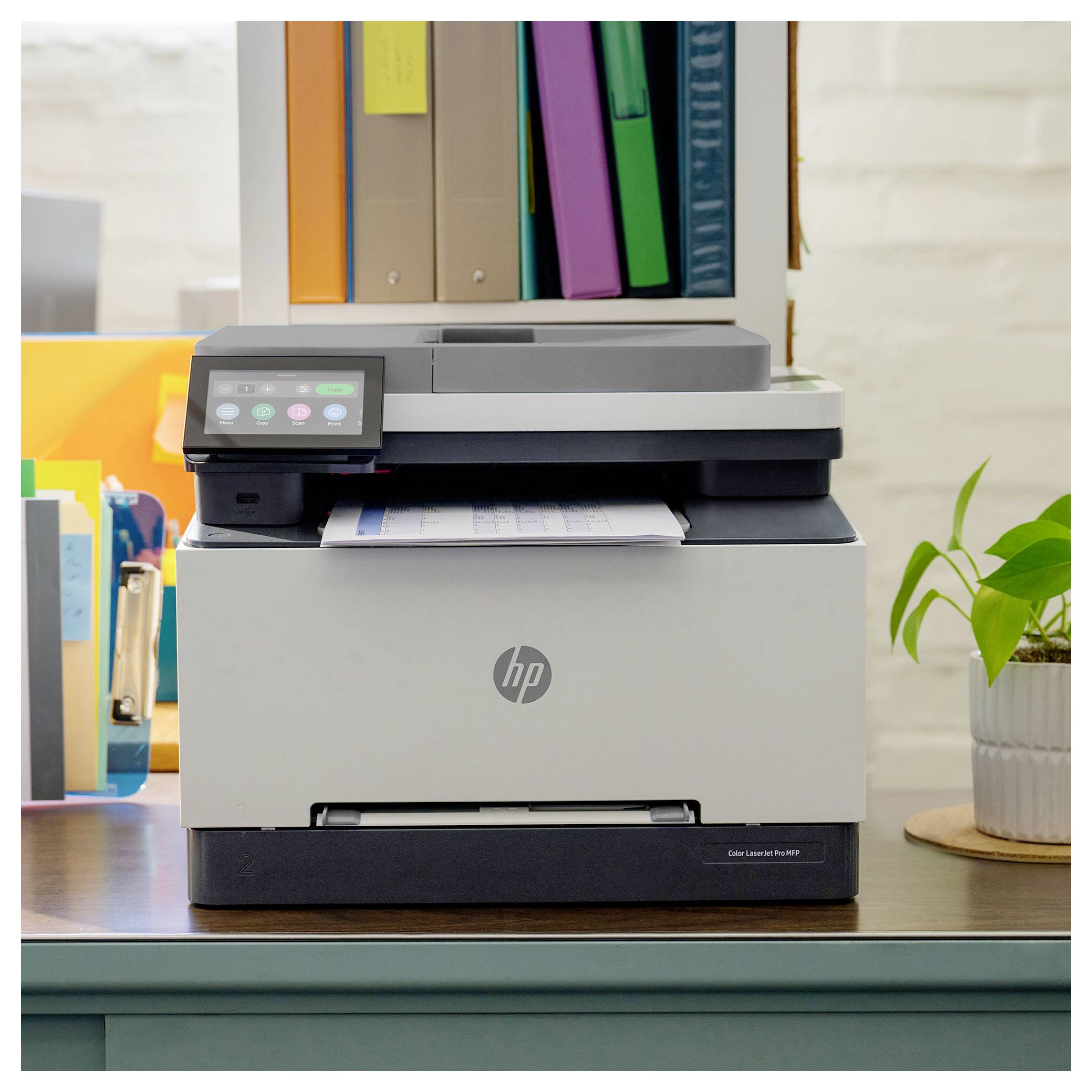HP multifunkční tiskárna na stole s naloženými dokumenty a kancelářskými složkami naskládanými nad ní.