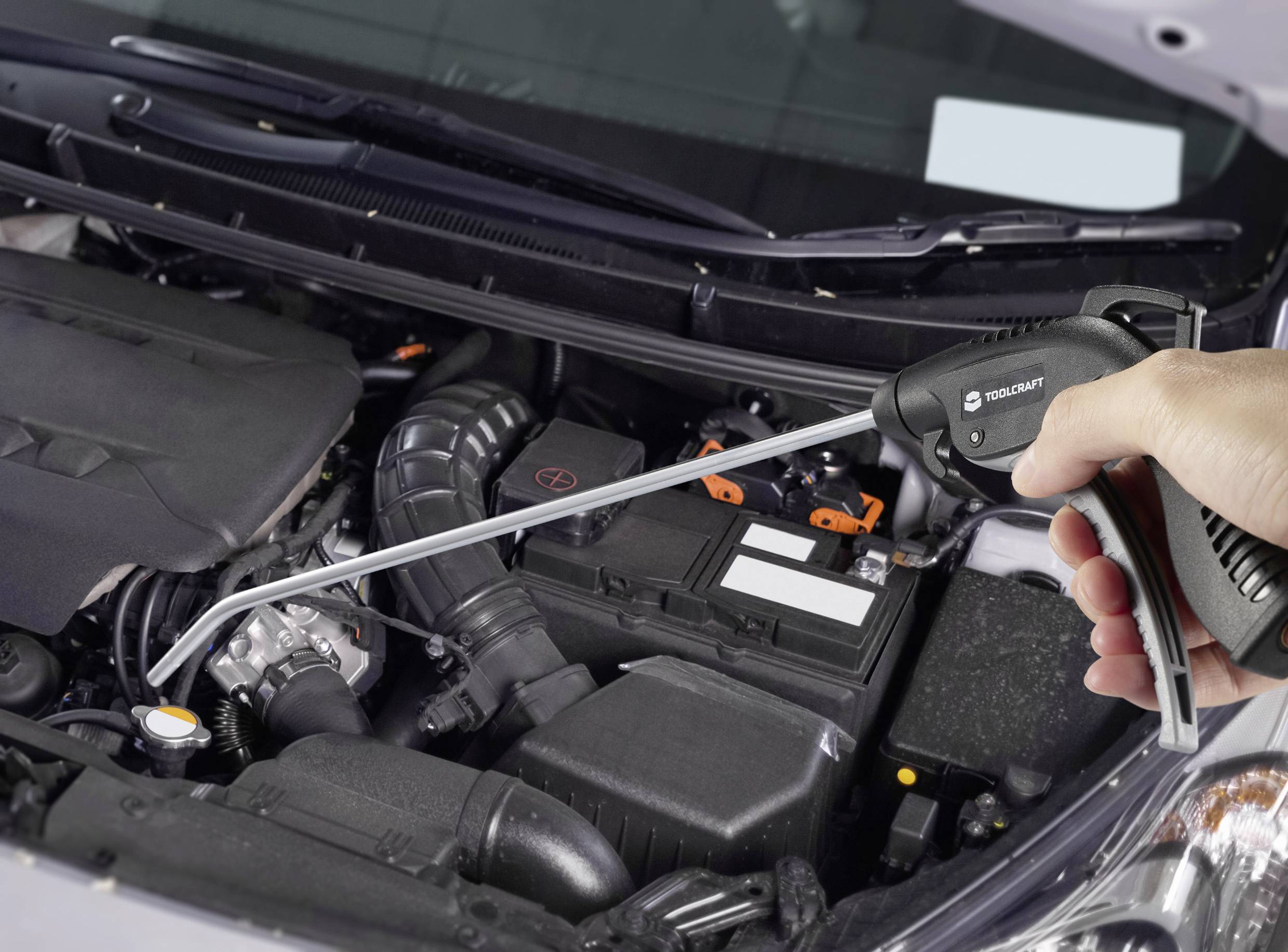 Ruka drží ofukovací pistoli nad otevřeným chladičem automobilu, připravena k čištění v motorovém prostoru.