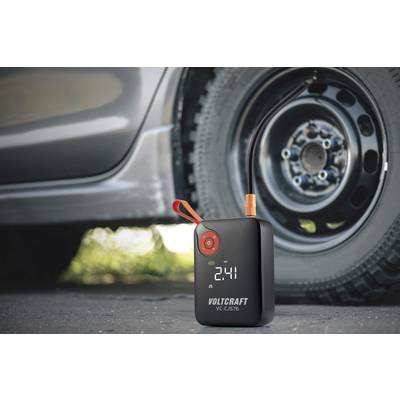 Přenosný kompresor na huštění pneumatik leží vedle autového kola a na displeji zobrazuje tlak '2.41', připravený k použití.