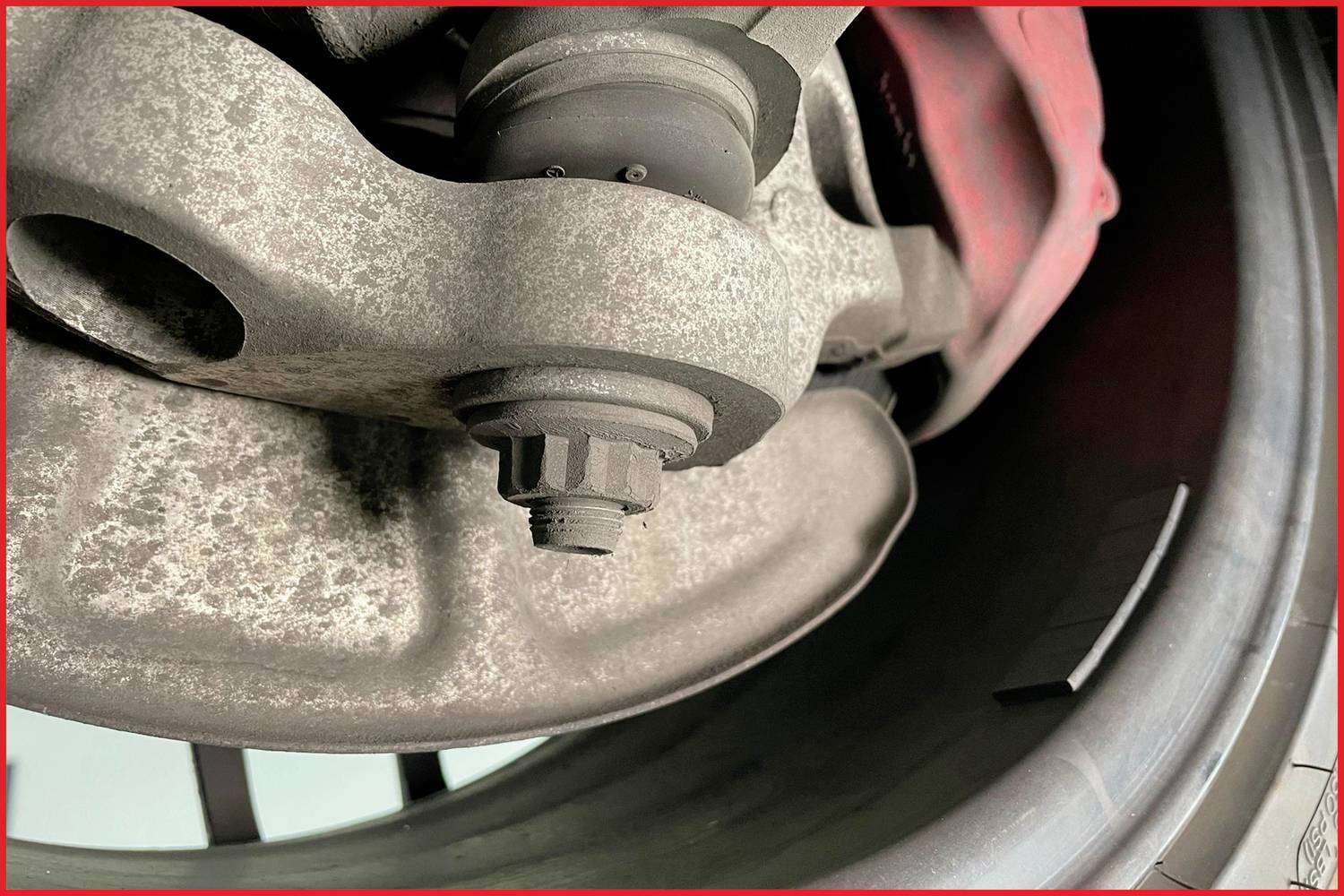 Detailní záběr rezavého automobilového kolového náboje s viditelným brzdovým třmenem vpravo.