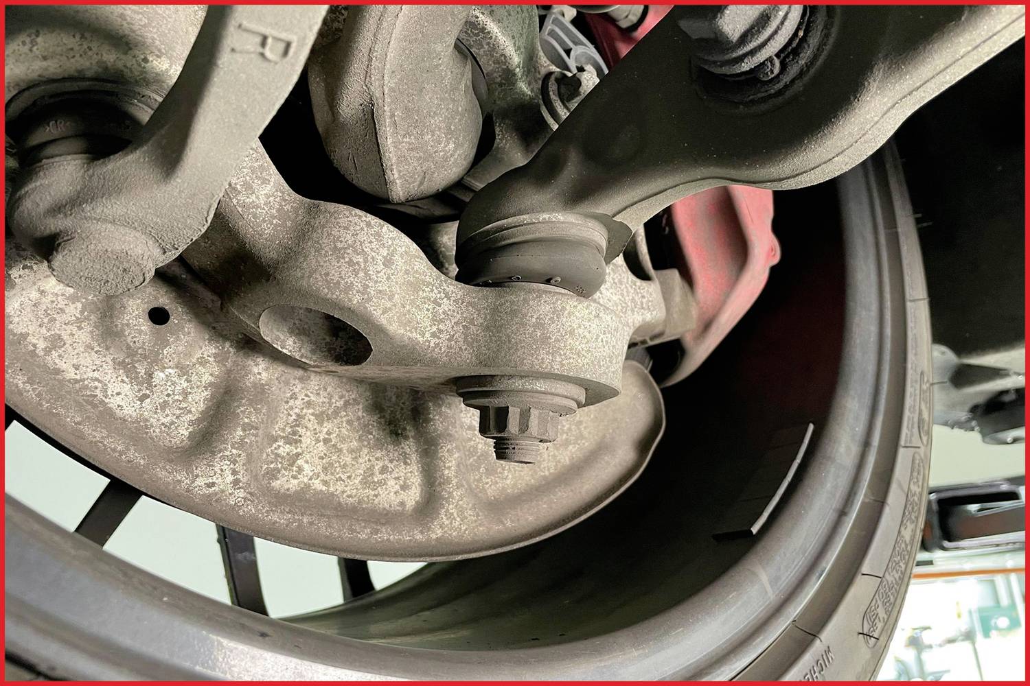 Detailní záběr pneumatiky automobilu a zavěšení v řezu, s viditelnými částmi brzdy. Zaměřeno na technické detaily.