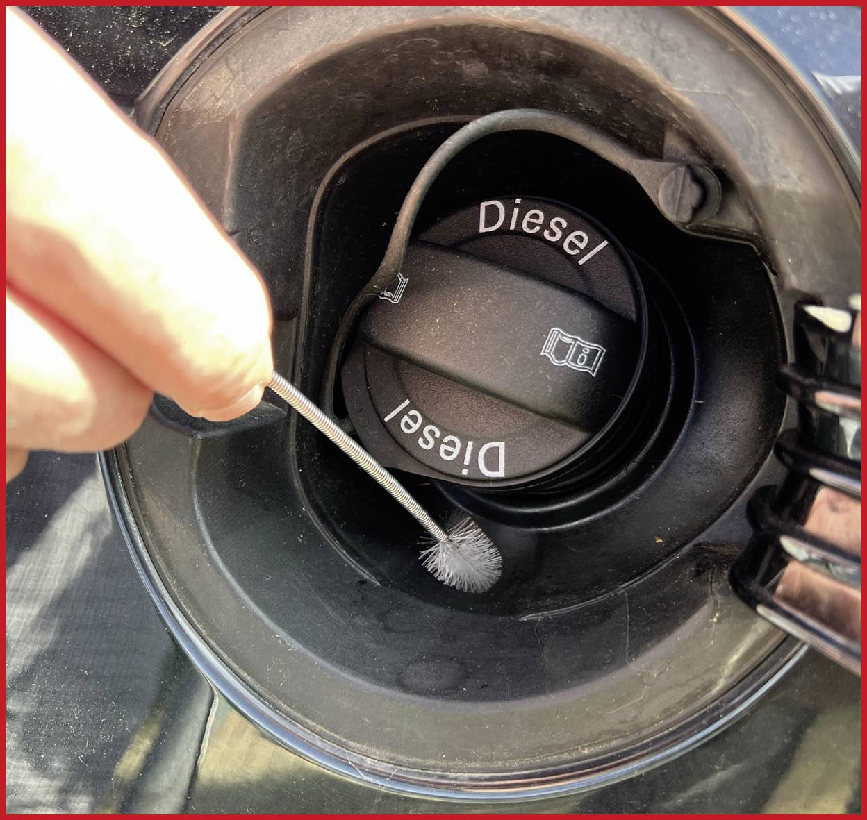 Ruka drží malý štětec a čistí vnitřní okraj víčka palivové nádrže automobilu s nápisem "Diesel".