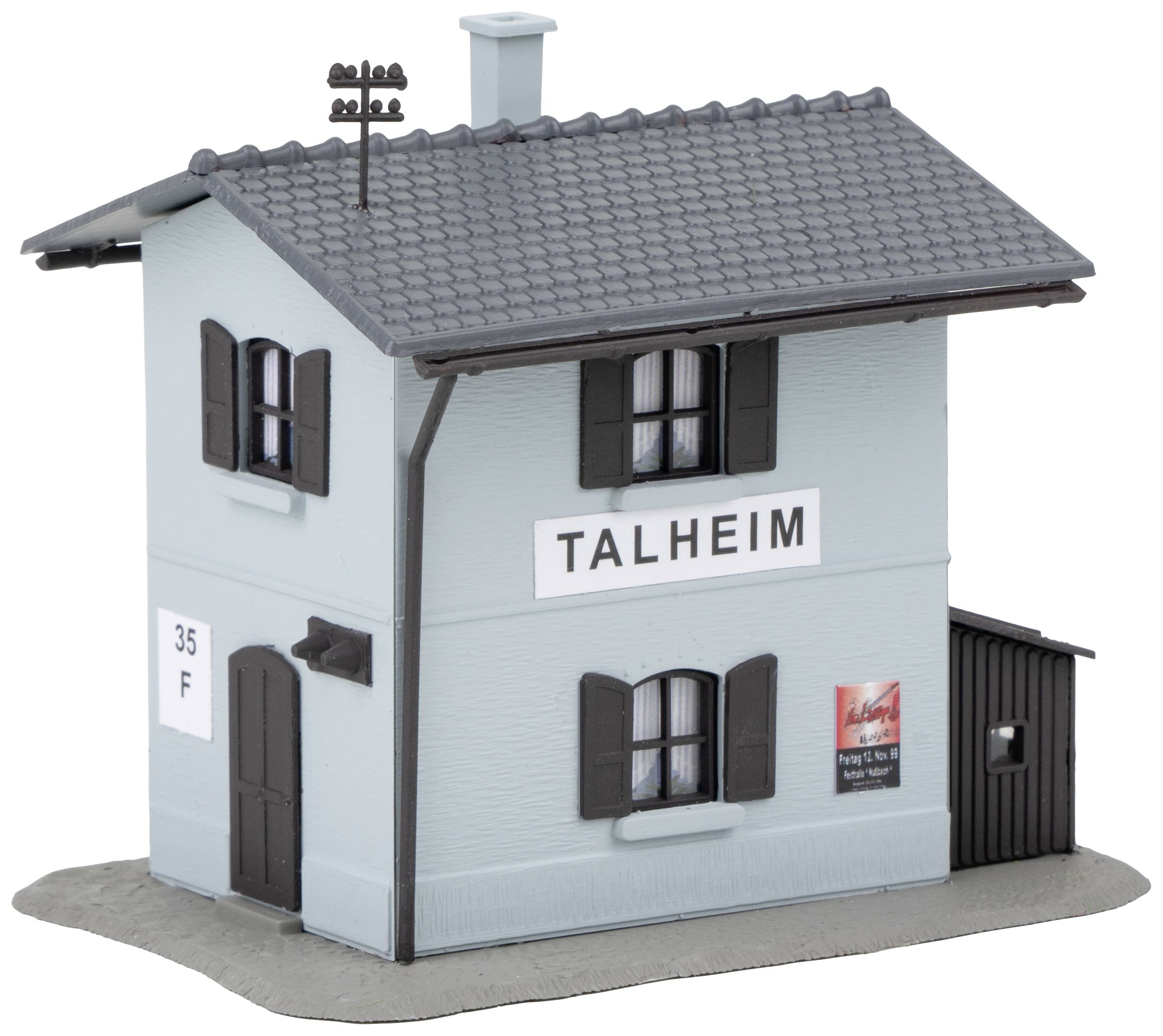 Malá modrá modelová budova s nápisem 'TALHEIM' na stěně, okenicemi a komínem. Hračka nebo dekorace do dioramatu.