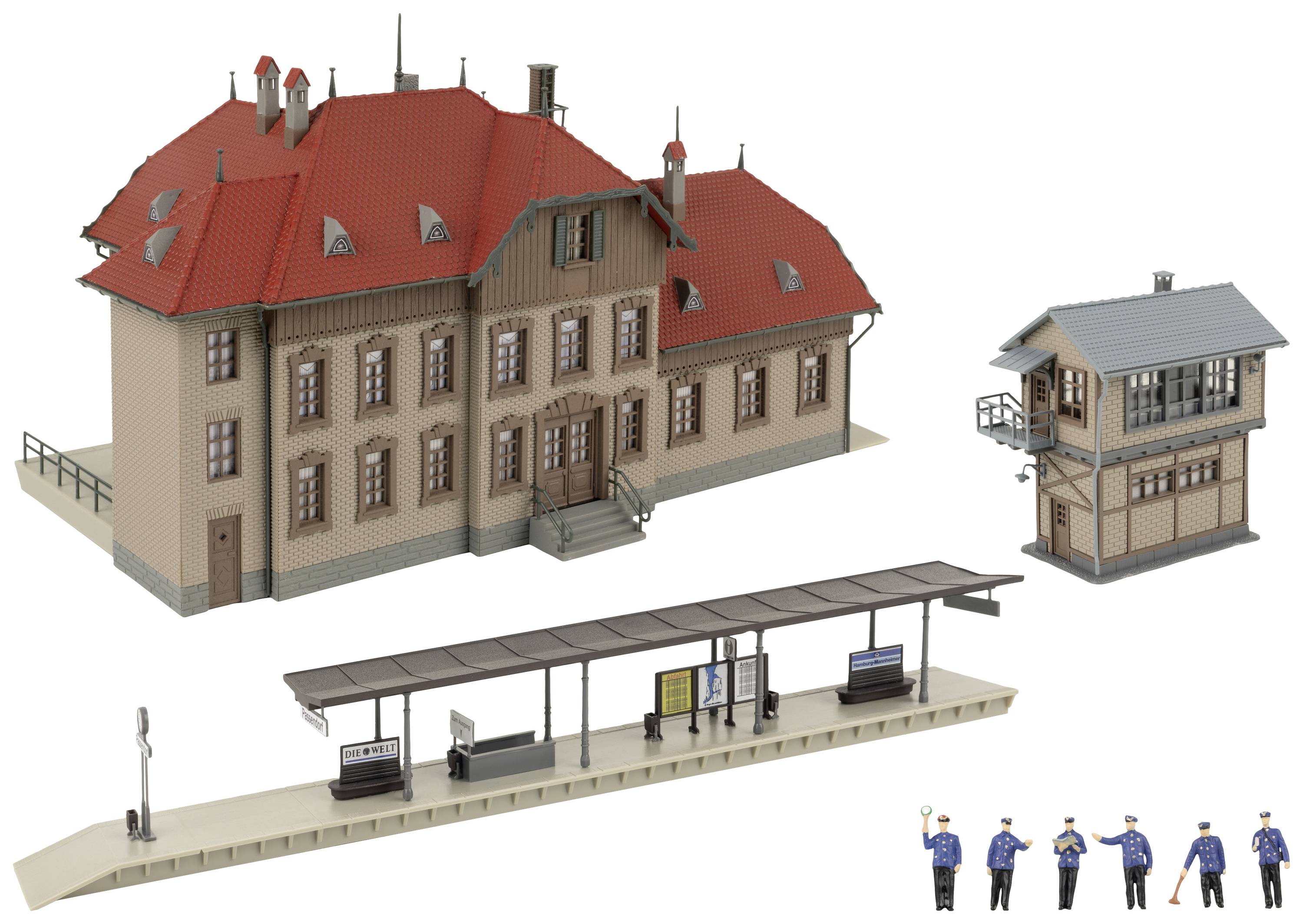 Modelové kolejiště s červenou střechou, nástupištěm, signalizačním zařízením a sadou figurek v uniformách.