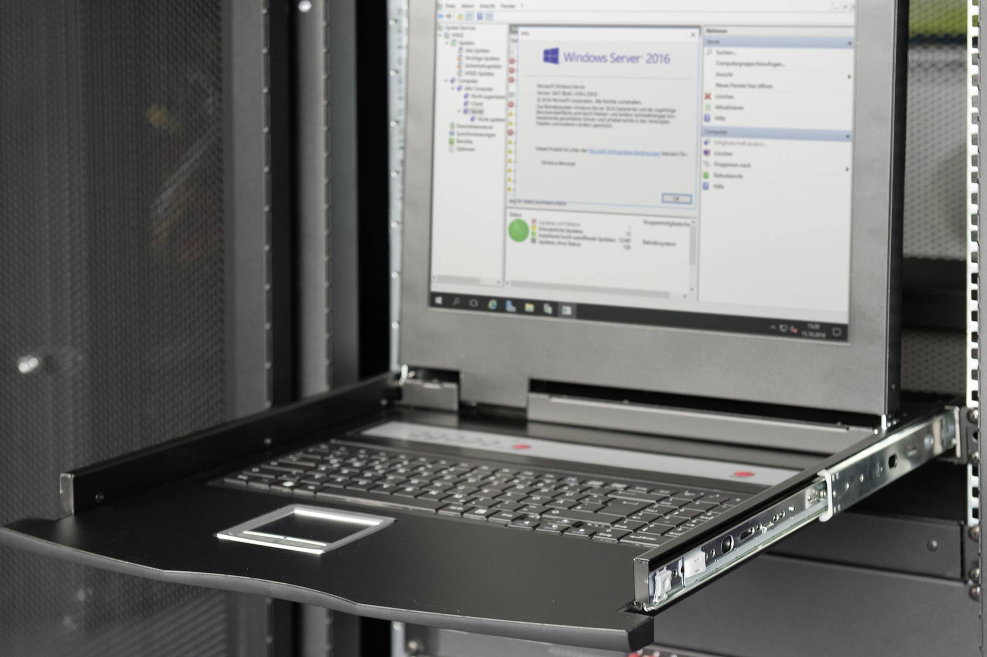 Serverová skříň s výsuvným konzolním monitorem zobrazujícím okno systému Windows Server 2016 s informacemi o systému.