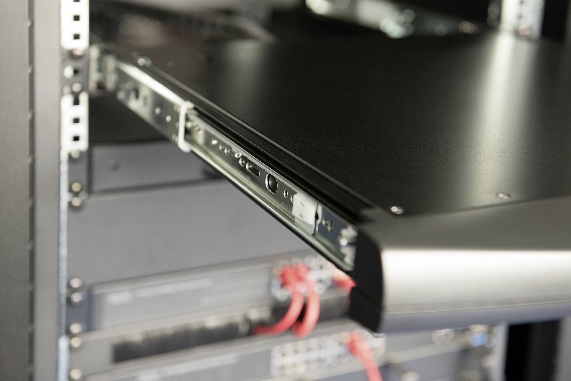 V serverovně je vidět vysunutý server v racku. Červené kabely jsou připojeny k dolním zařízením.