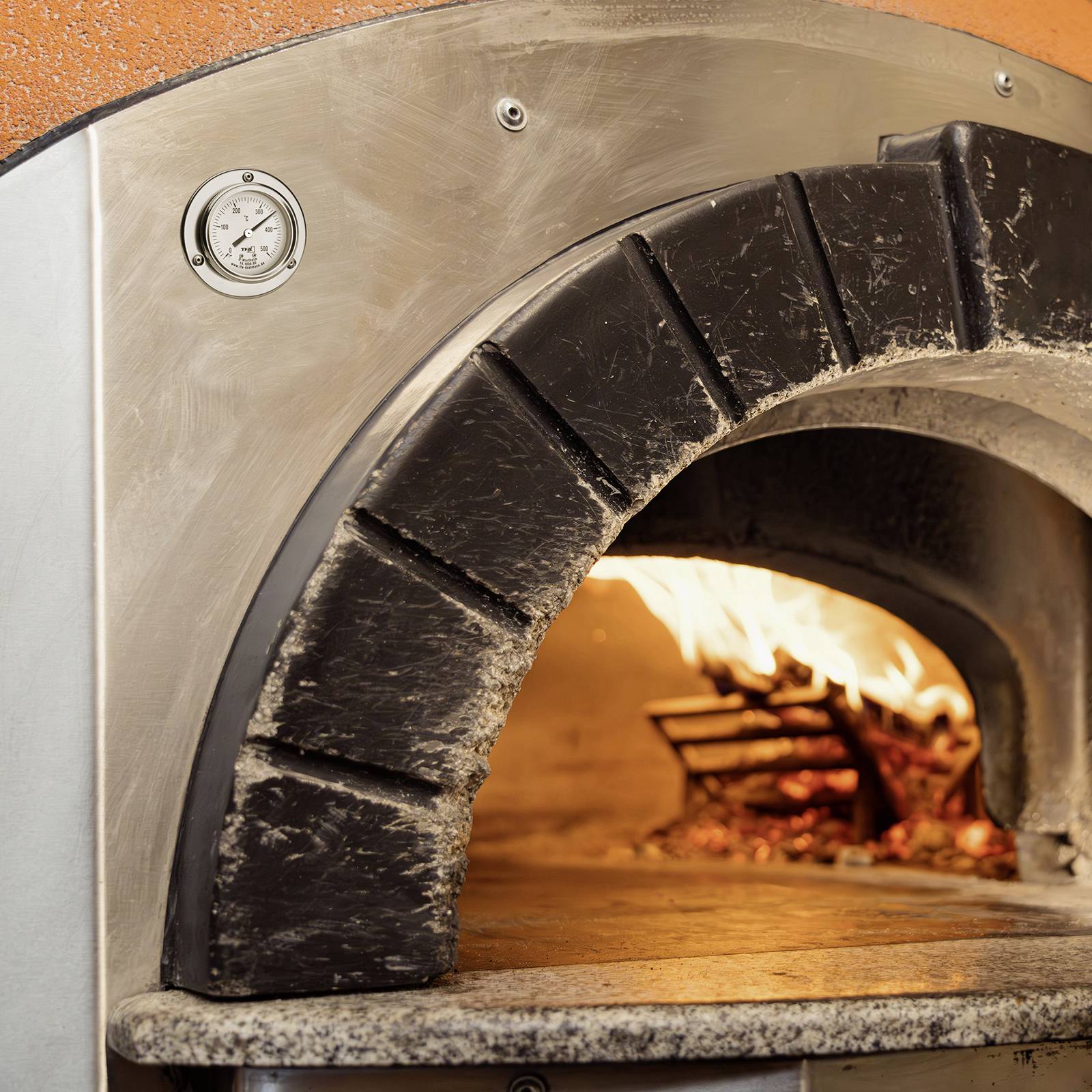 Tradiční dřevěná pec s hořícím dřevem a plameny, vhodná pro pečení pizzy nebo chleba.