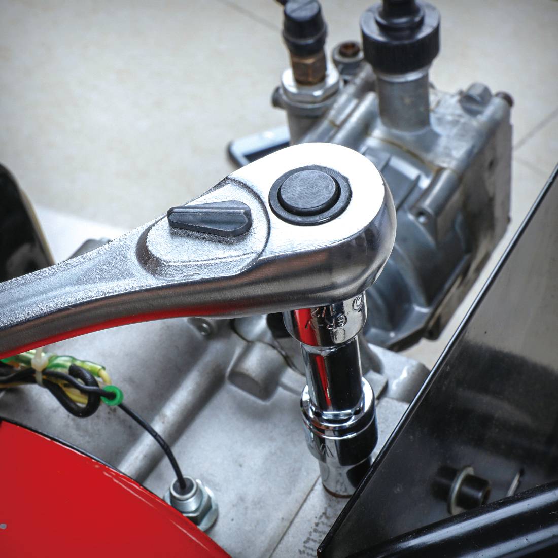 Detailní záběr nástrčného klíče, který povoluje nebo utahuje matici. V pozadí je viditelný strojní motor.