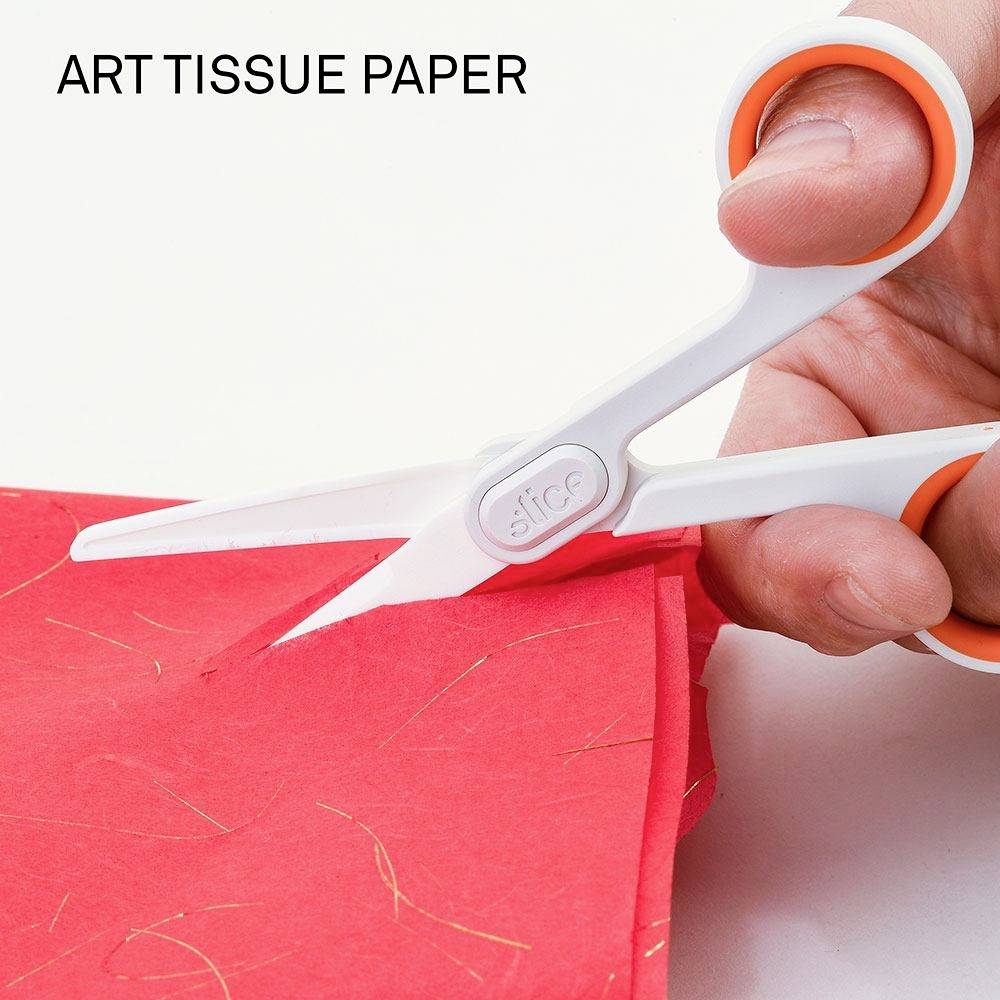 Jedna ruka drží bílé nůžky s oranžovými rukojeťmi a stříhá červený hedvábný papír. Vlevo nahoře je napsáno 'ART TISSUE PAPER'.