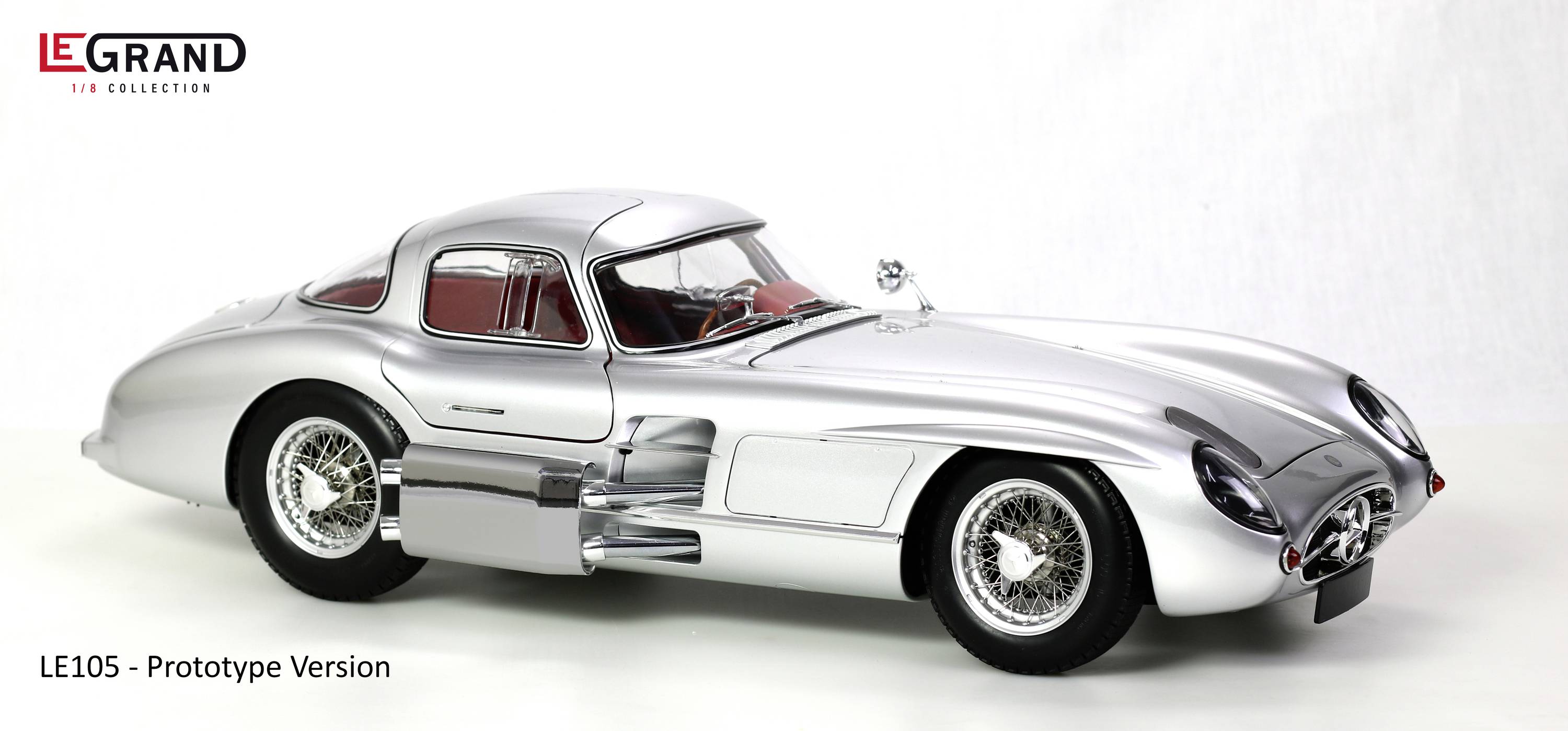 Stříbrný modelový automobil v retro designu s červeným interiérem, pohled z boku. Je označen jako 'LE105 - Prototypová verze'.