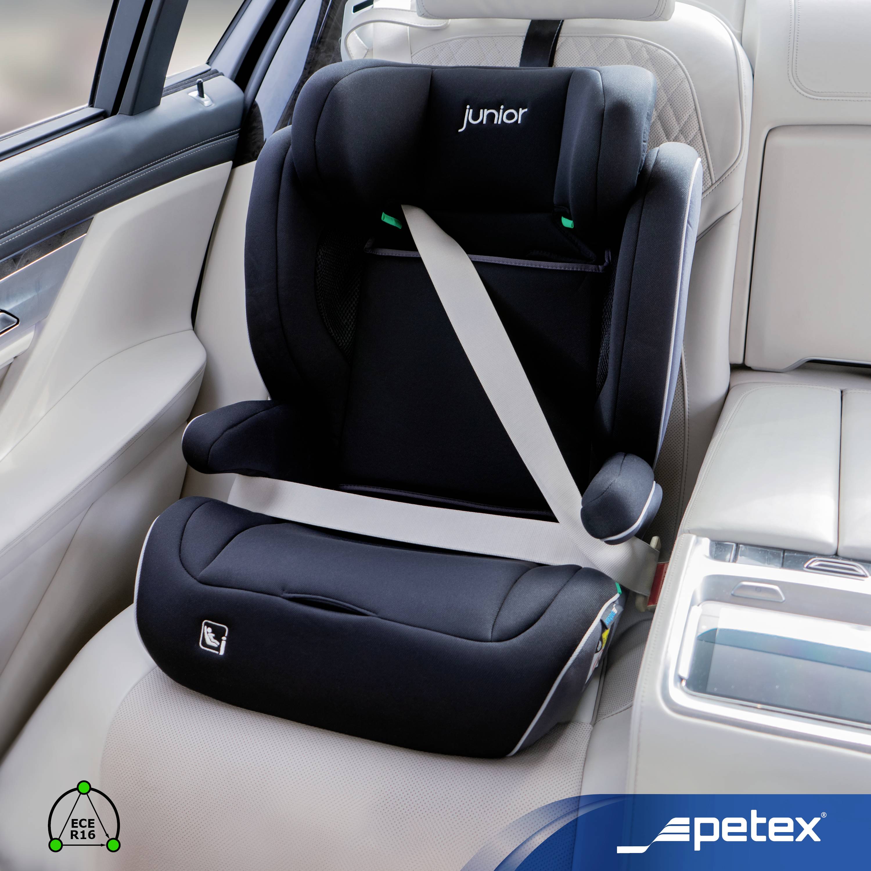 Černá dětská autosedačka 'junior' s bezpečnostním pásem je namontována na béžovém sedadle automobilu. V popředí je viditelné logo 'petex'.