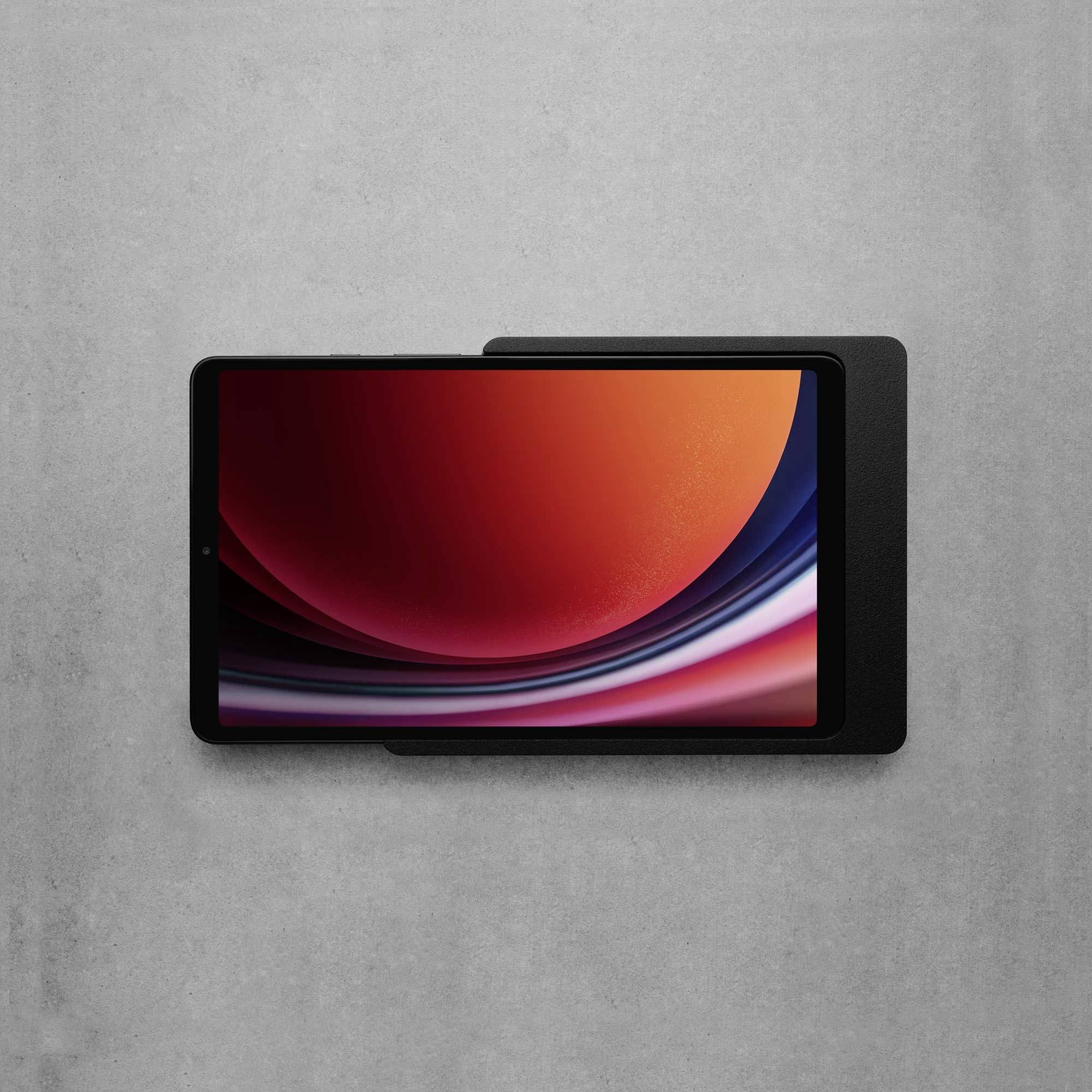 Tablet s barevným displejem zobrazujícím abstraktní červeno-černou grafiku leží na šedém povrchu.