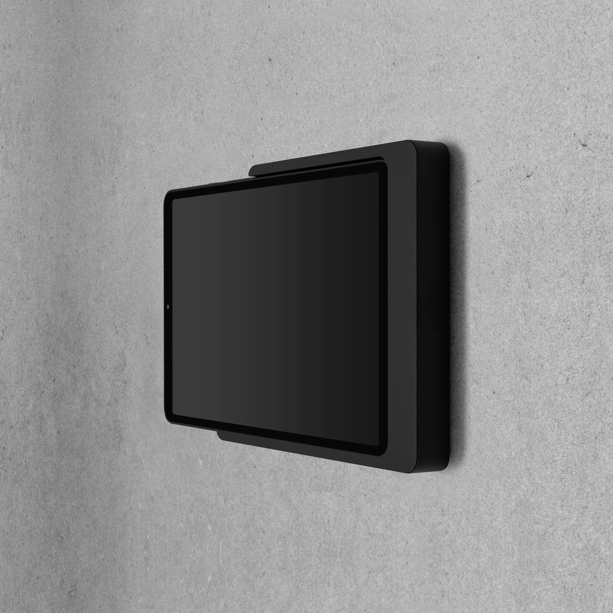 Tablet je připevněn na šedé zdi na šířku, s černým rámečkem a černou obrazovkou.