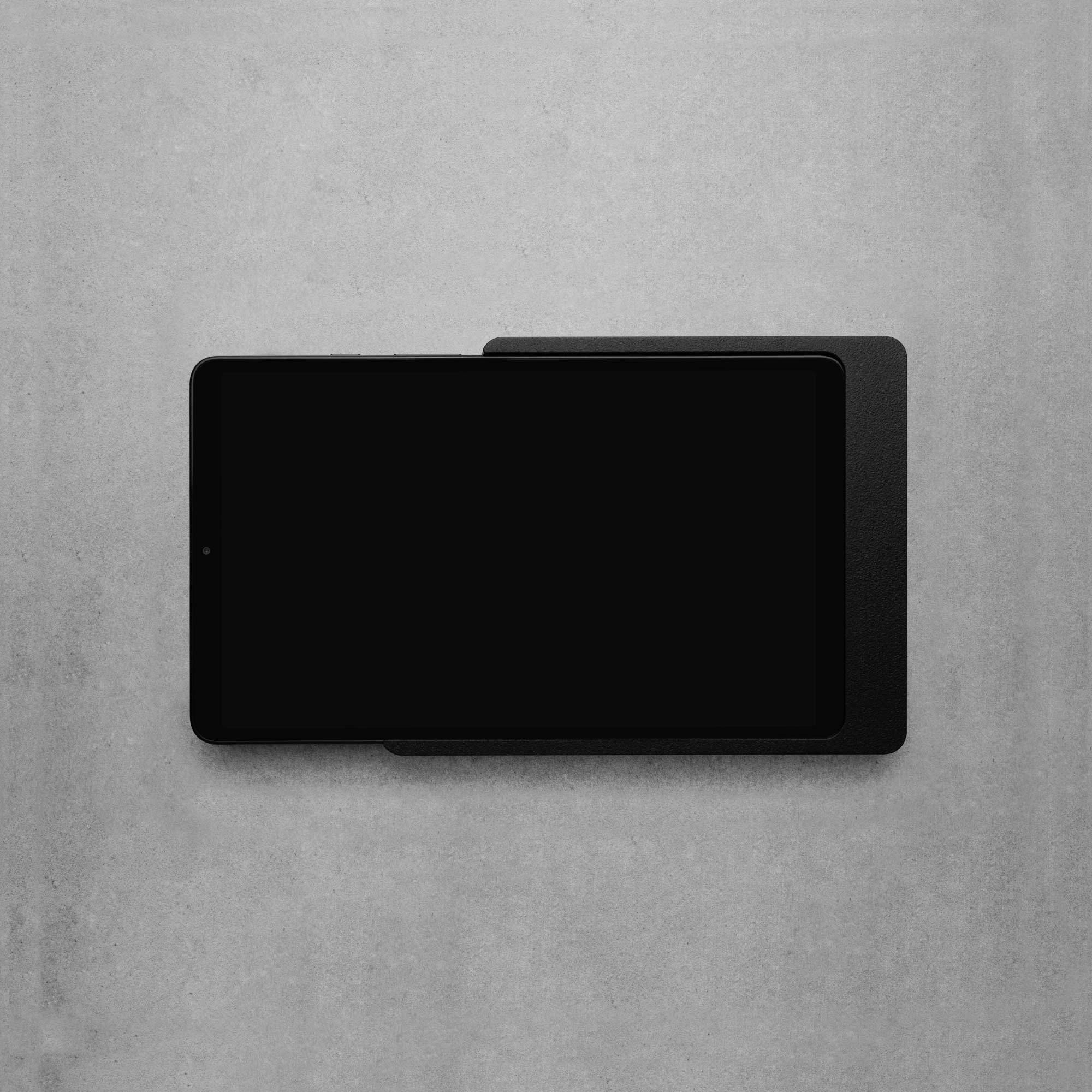 Černý tablet leží na šedém pozadí. Zobrazuje černou obrazovku bez viditelného obsahu nebo detailů.