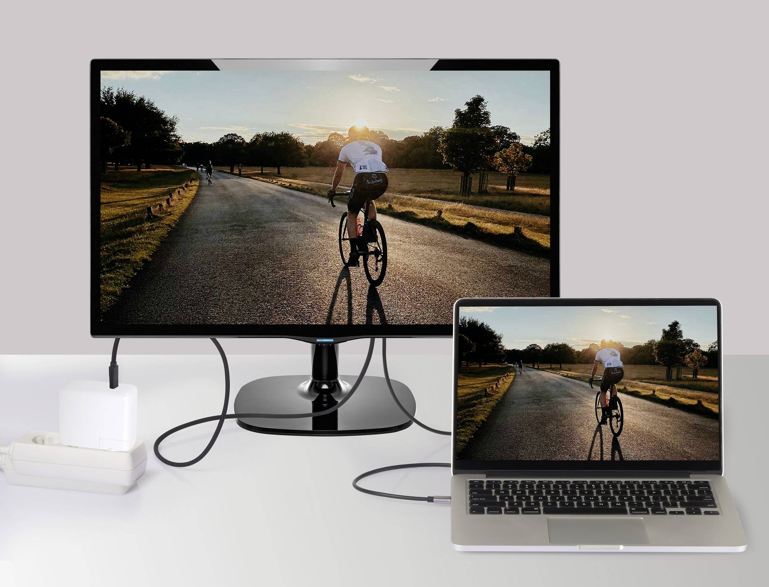 Laptop je připojený k většímu monitoru a na obou obrazovkách je vidět obrázek cyklisty na silnici při západu slunce.