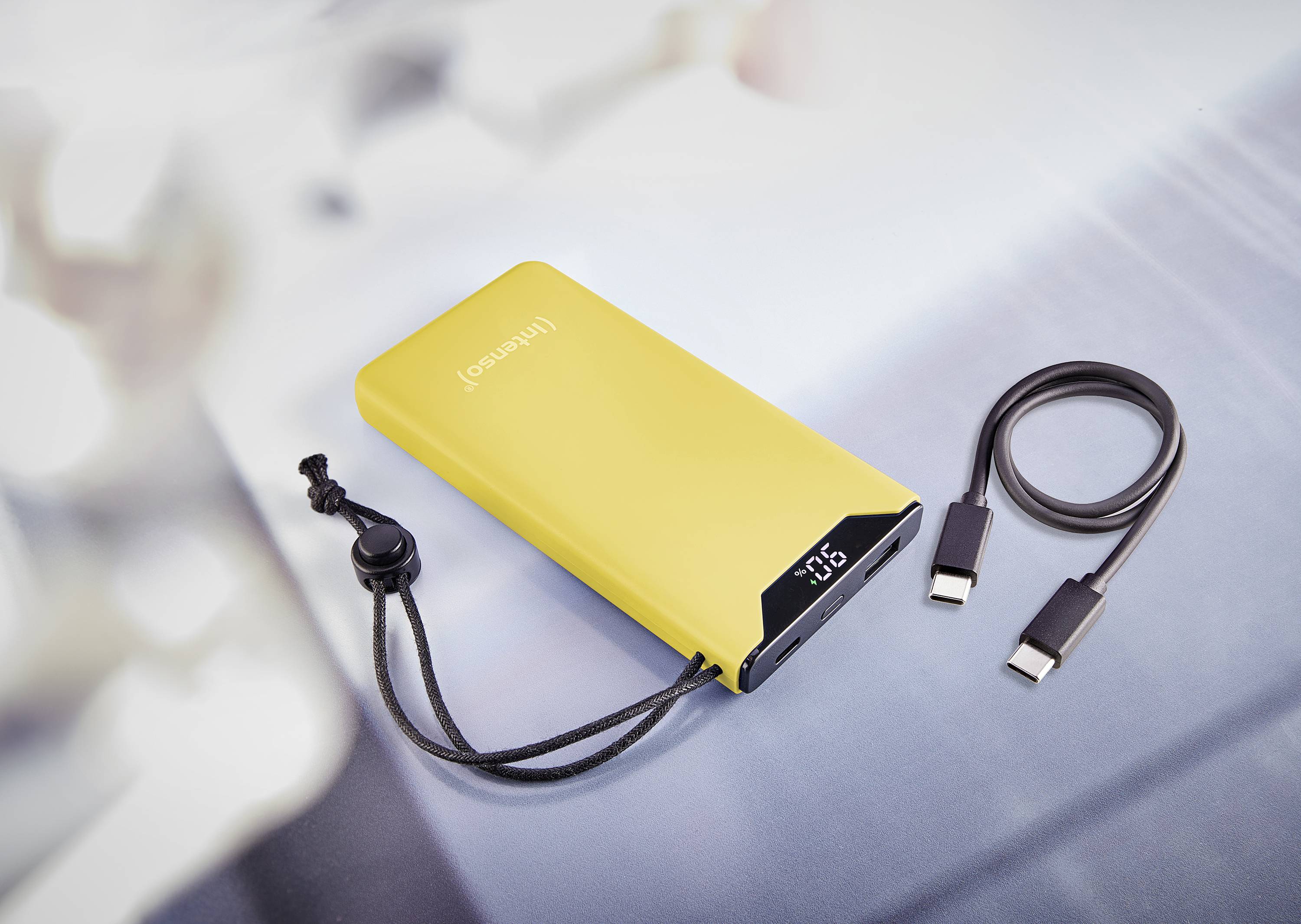 Žlutá powerbanka s digitálním displejem zobrazuje stav nabití. Vedle ní leží nabíjecí kabel se dvěma konektory.