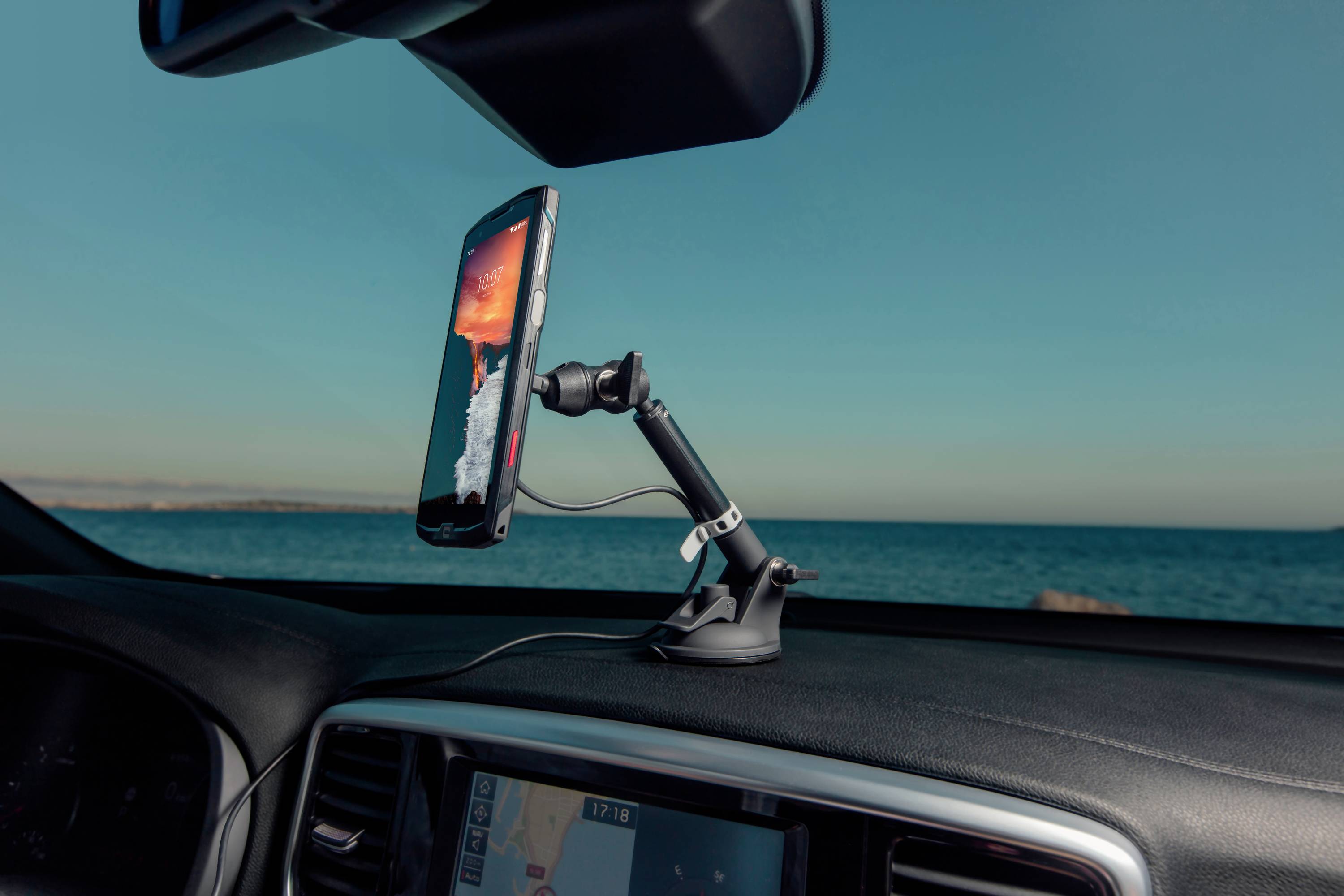 Smartphone v držáku na palubní desce, přehrává video. V pozadí moře pod jasnou oblohou.
