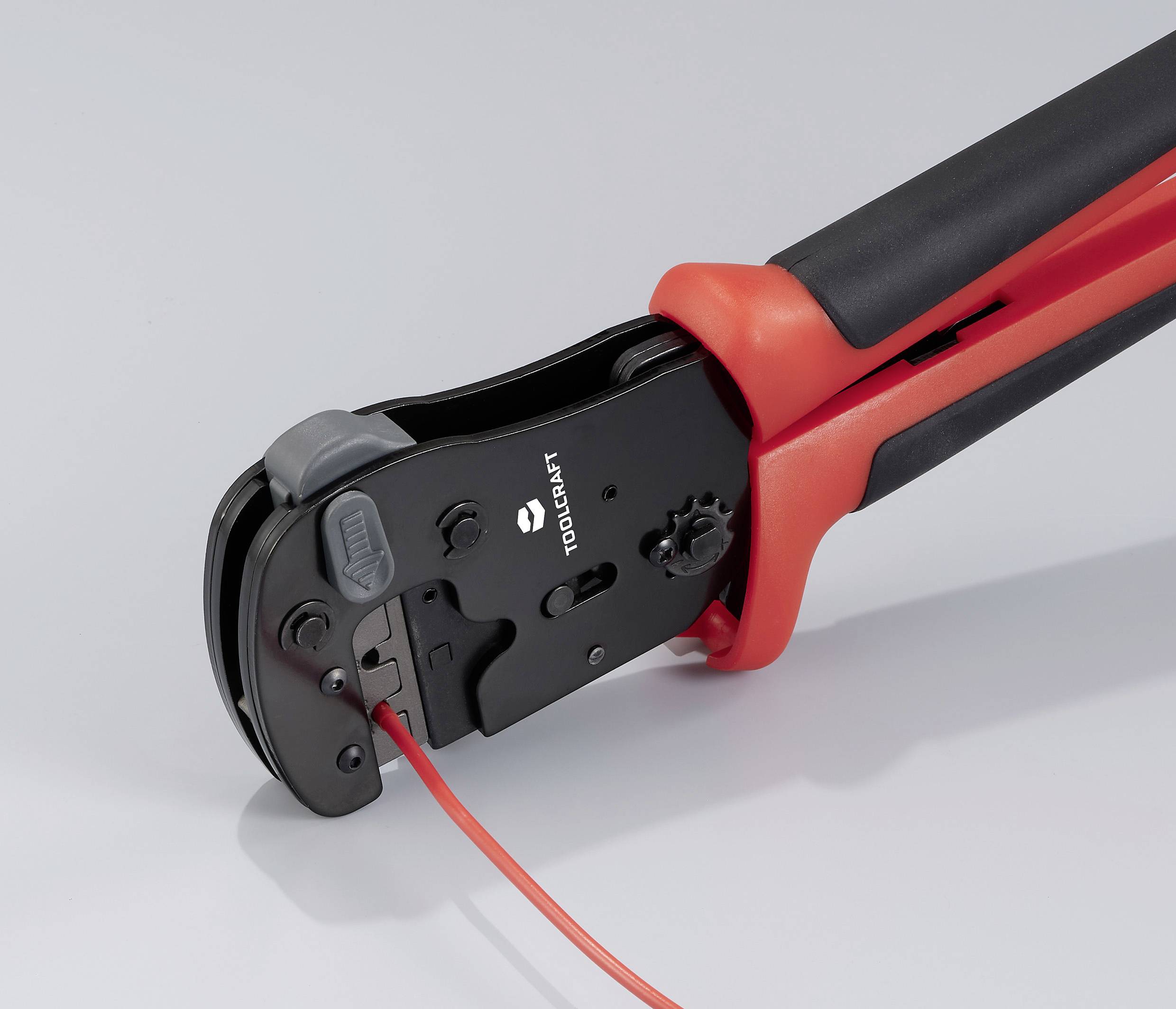 Kleště na krimpování, převážně černé s červenými rukojeťmi, drží červený kabel a jsou připravené ke krimpování. Vhodné pro elektrotechnické práce.