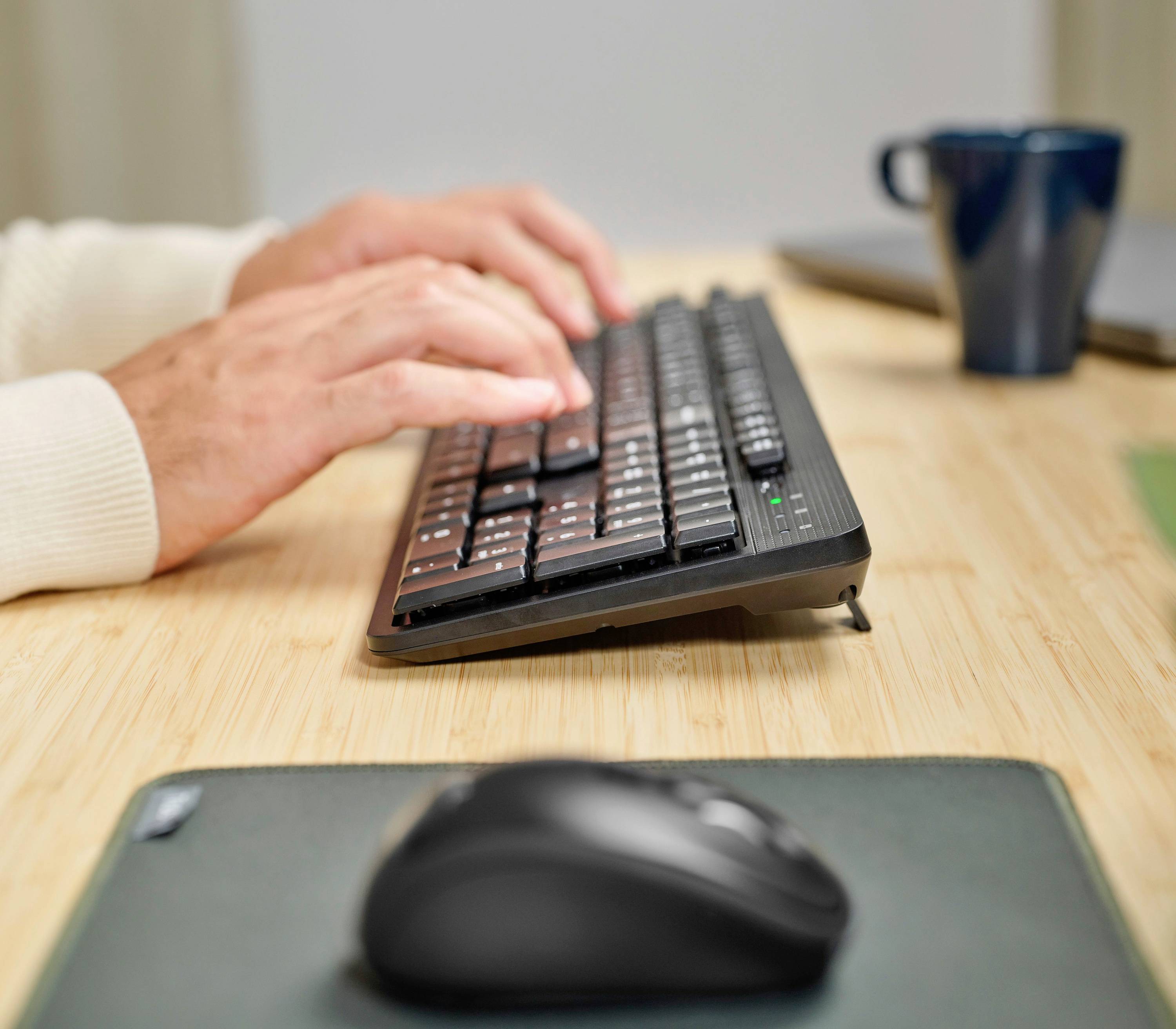 Notebook s částečně otevřenou klávesnicí v kanceláři, ruka osoby ovládá touchpad, zaměření na klávesnici a prsty.