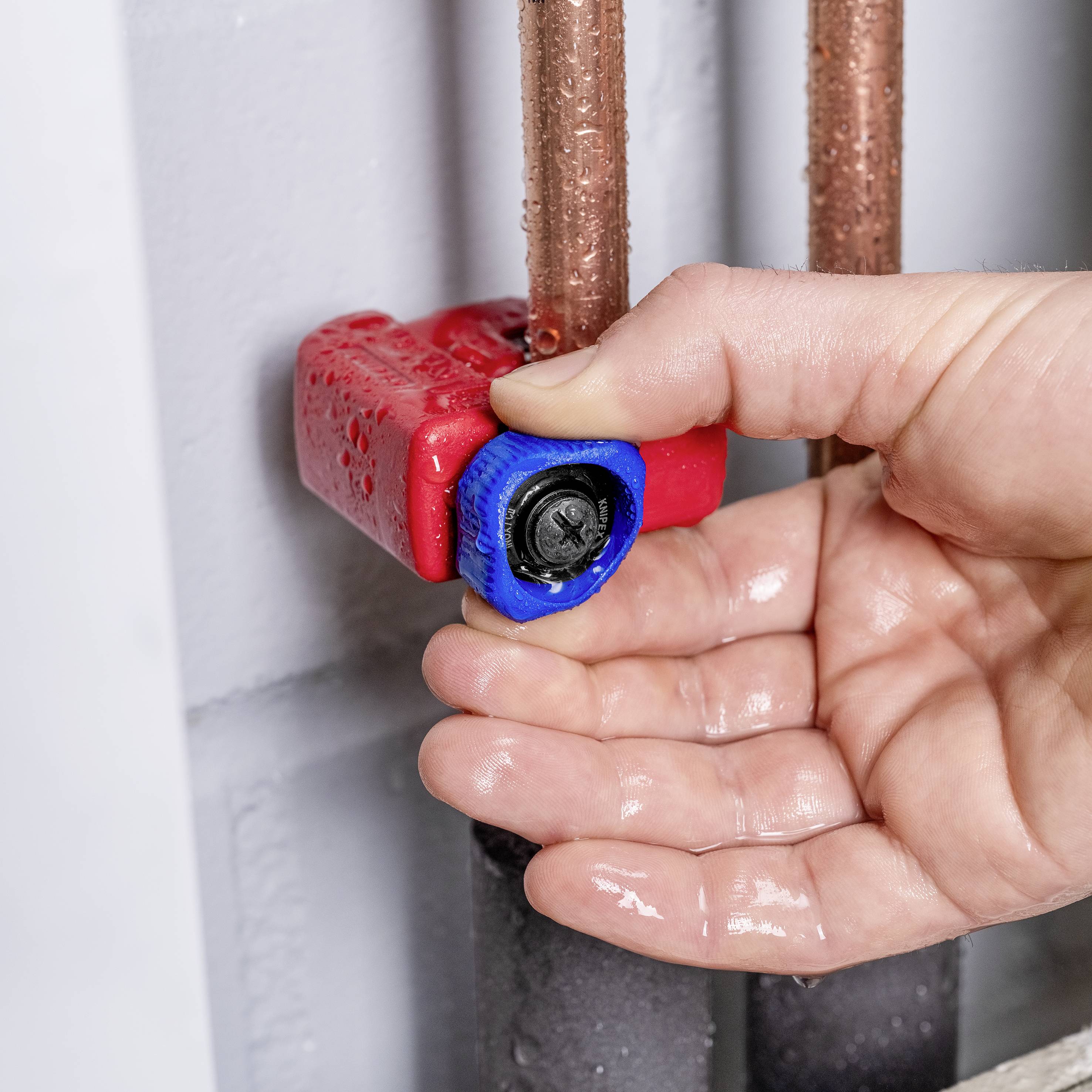 Ruka otáčí červeno-modrým ventilem na měděných trubkách, aby upravila přívod vody.