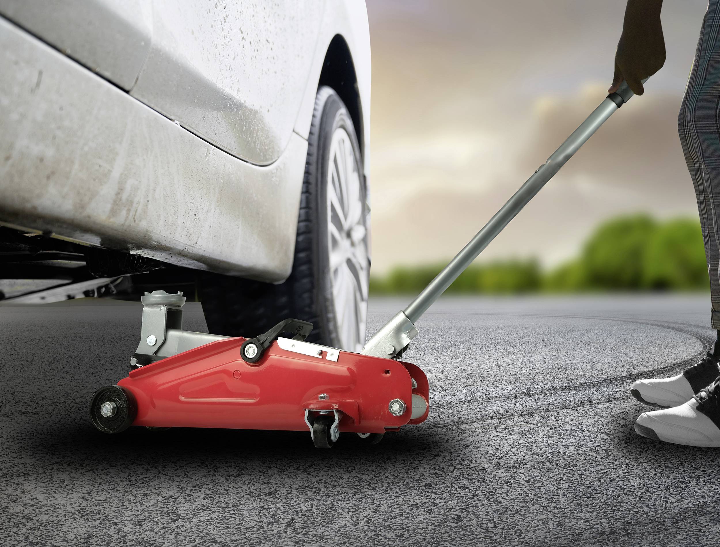 Jedna osoba používá zvedák, aby zvedla automobil. Zvedák je červený a nachází se pod autem.