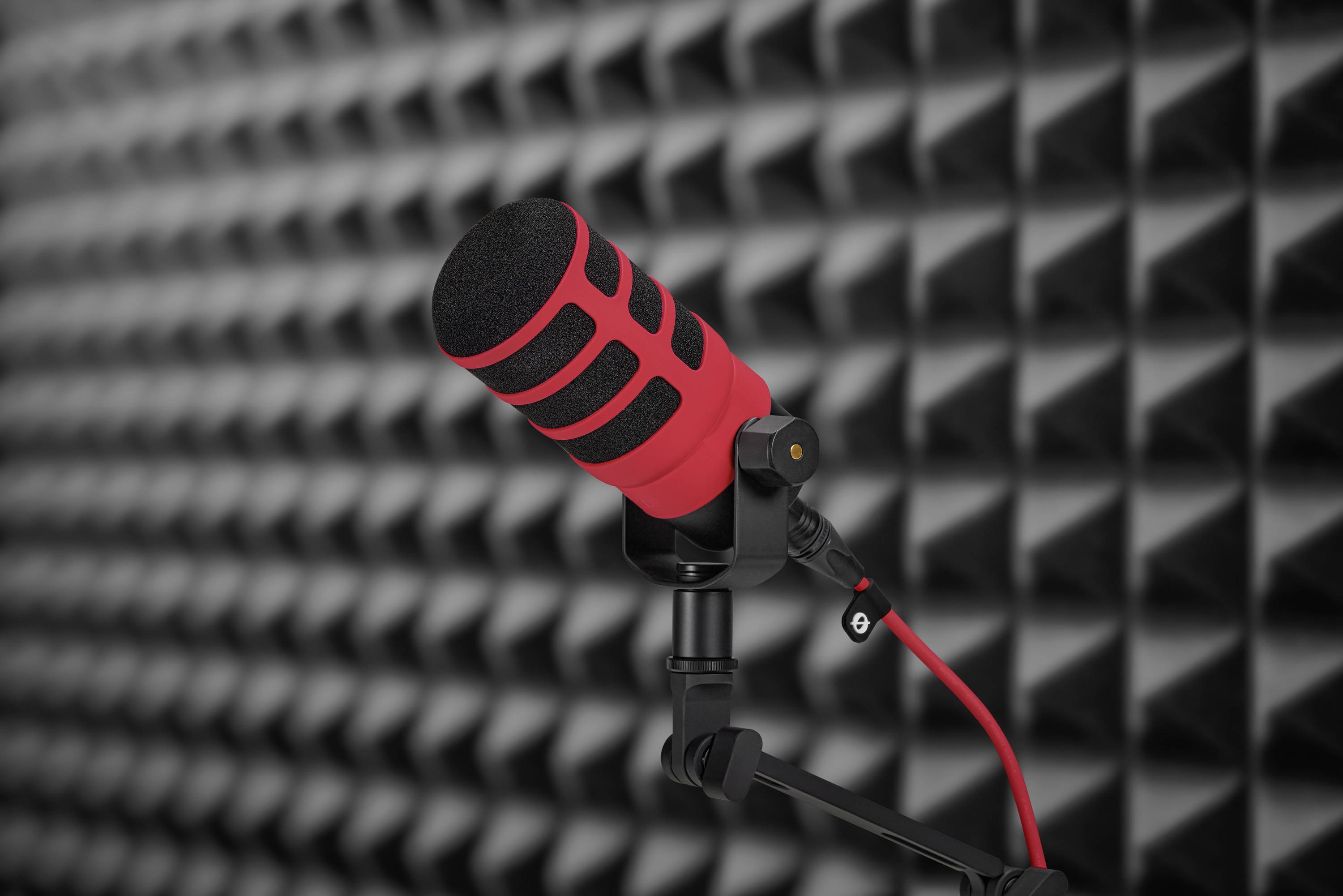 Červený mikrofon v akusticky izolované místnosti, upevněný na stojanu. Ideální pro audio nahrávky bez rušivých zvuků.