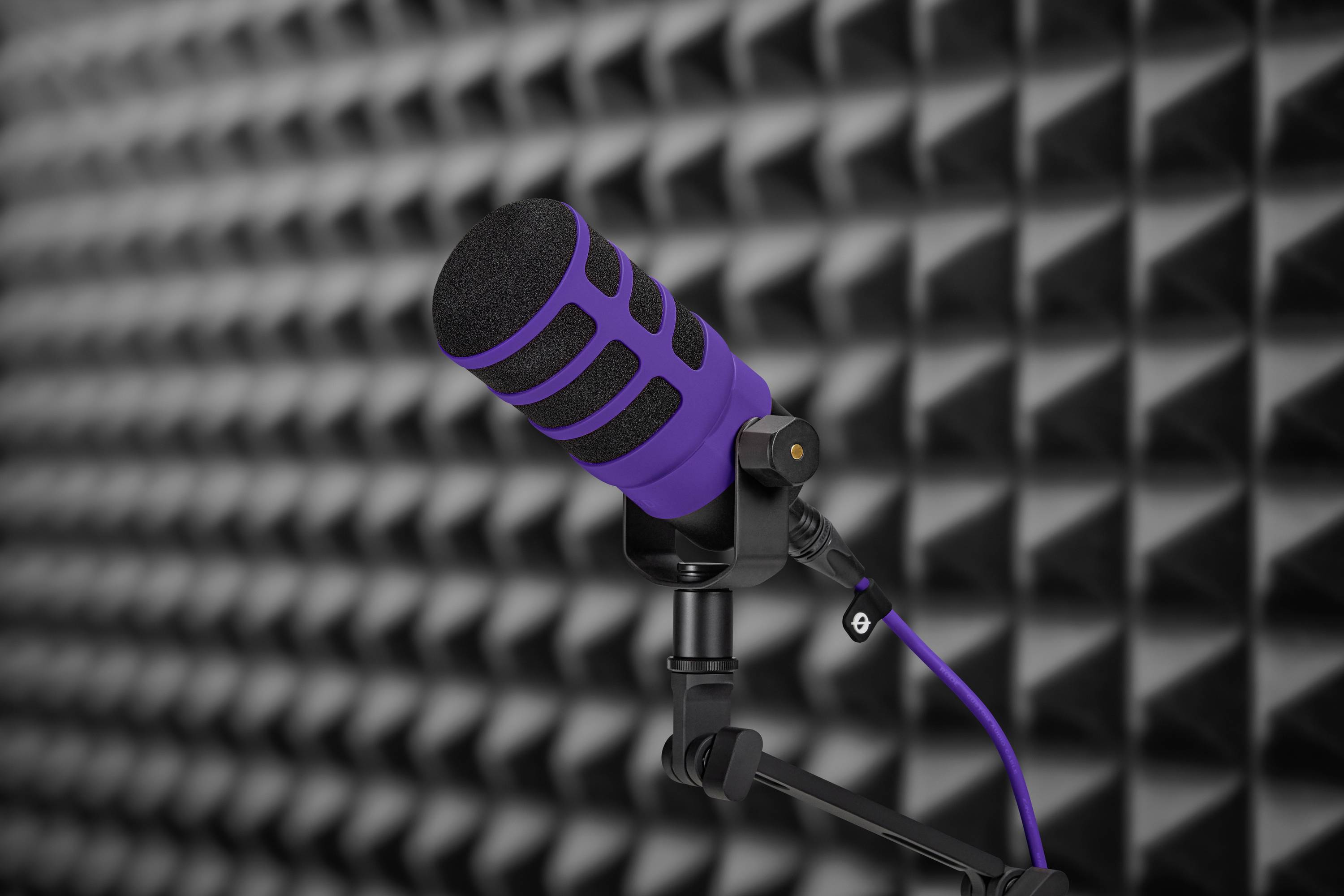 Fialový mikrofon na stojanu před zvukově izolovanou stěnou, připravený na nahrávání nebo podcast.