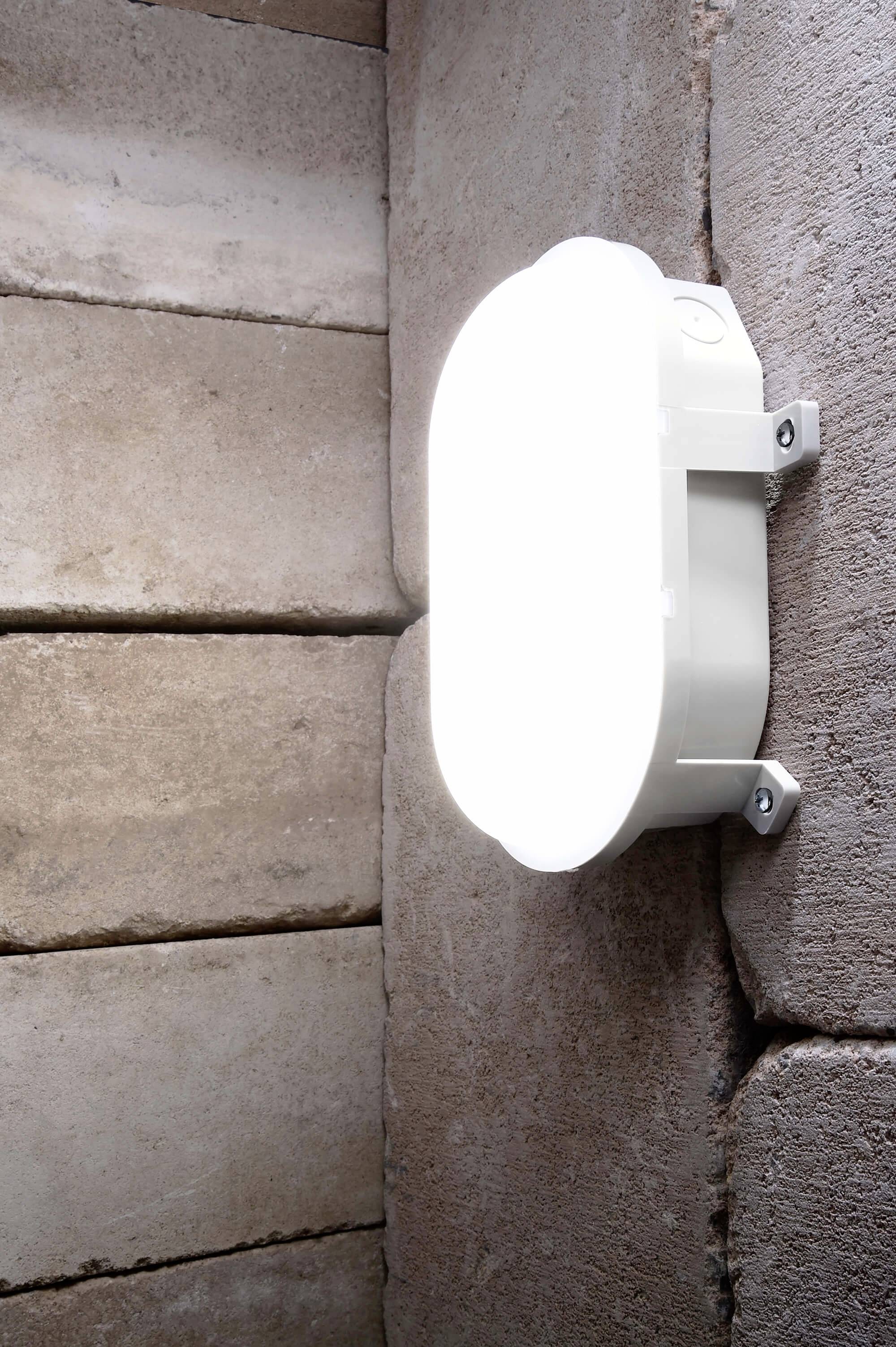 Zářivá oválná lampa na světle hnědé cihlové zdi. Lampa vyzařuje jasné světlo, osvětluje okolní kameny.
