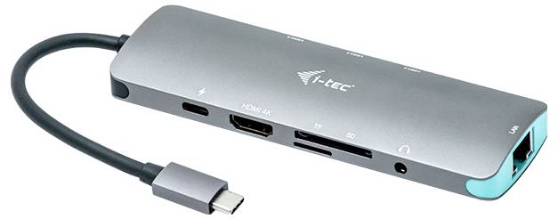 Stříbrný USB-C hub s několika porty, včetně HDMI, USB, LAN a čtečky SD karet, na bílém pozadí.